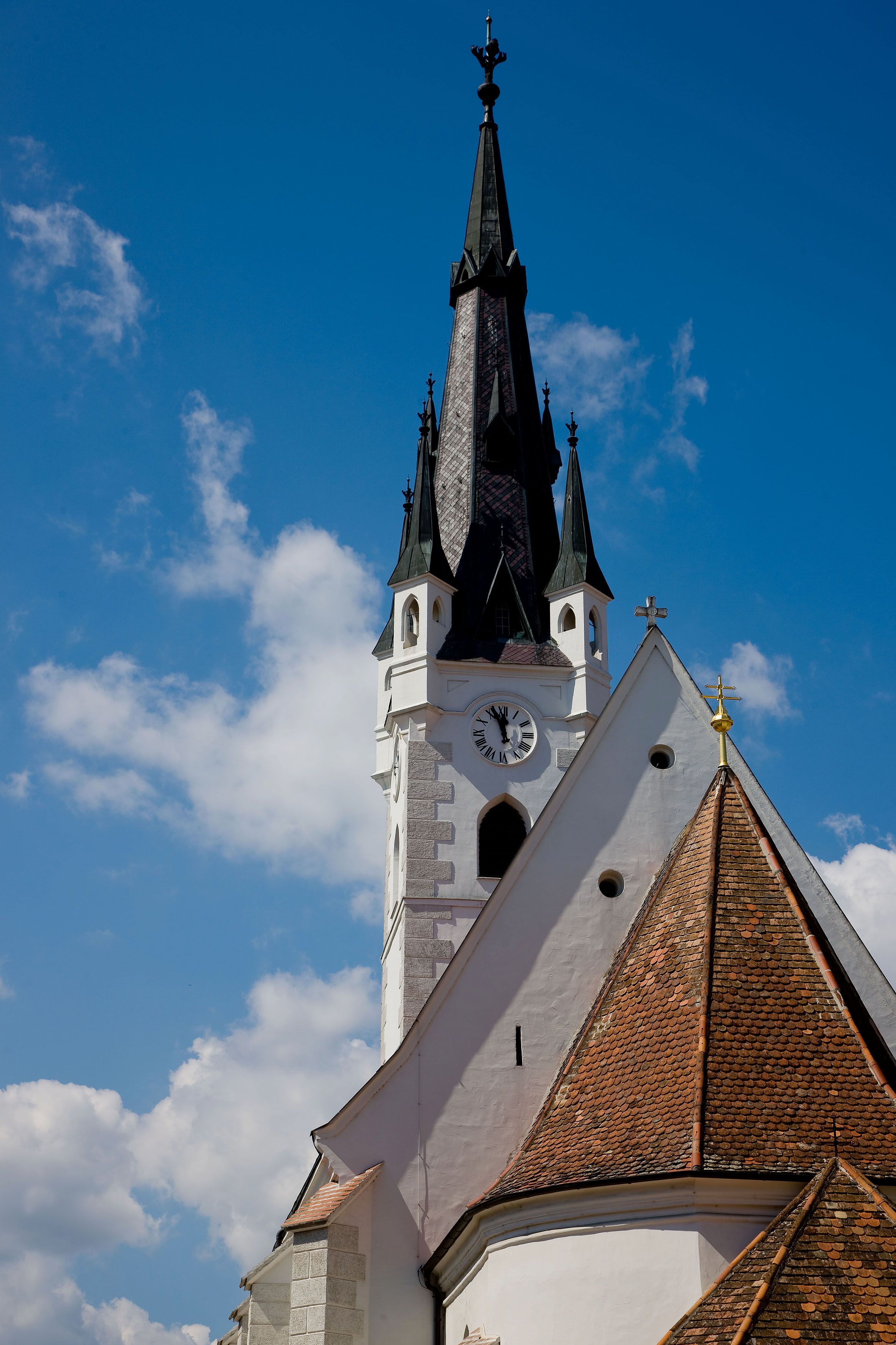 Church tower with clock and pointed roof against a blue sky.