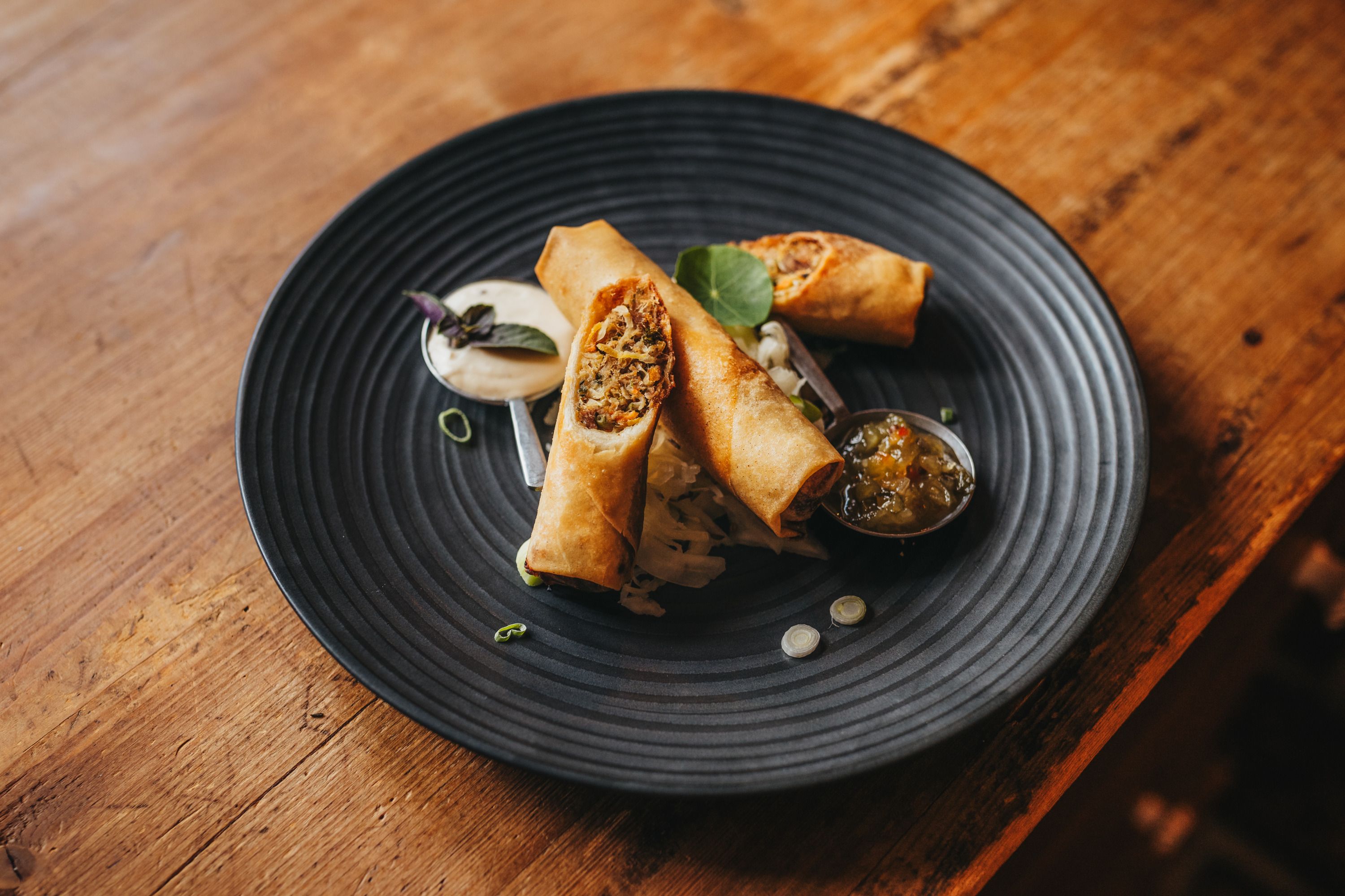 Fried spring roll with bacon cabbage and wasabi served on a black plate.