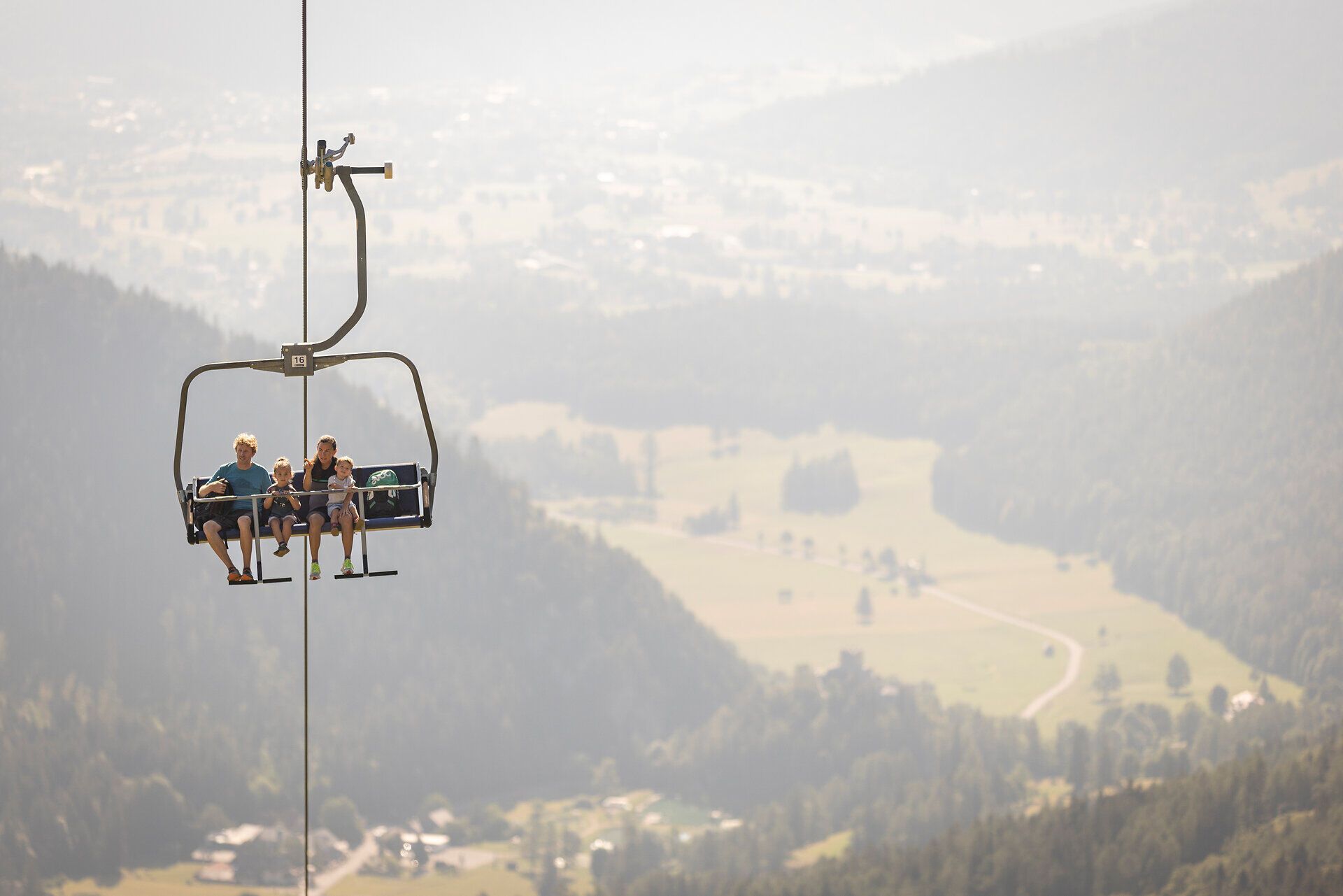 Nestled in the gentle embrace of the Vienna Alps, cheerful family members ride up on a chair lift. The breathtaking view of the surrounding valleys and mountains promises an unforgettable hiking adventure. Here, where nature blooms in all its glory, every moment becomes an experience.