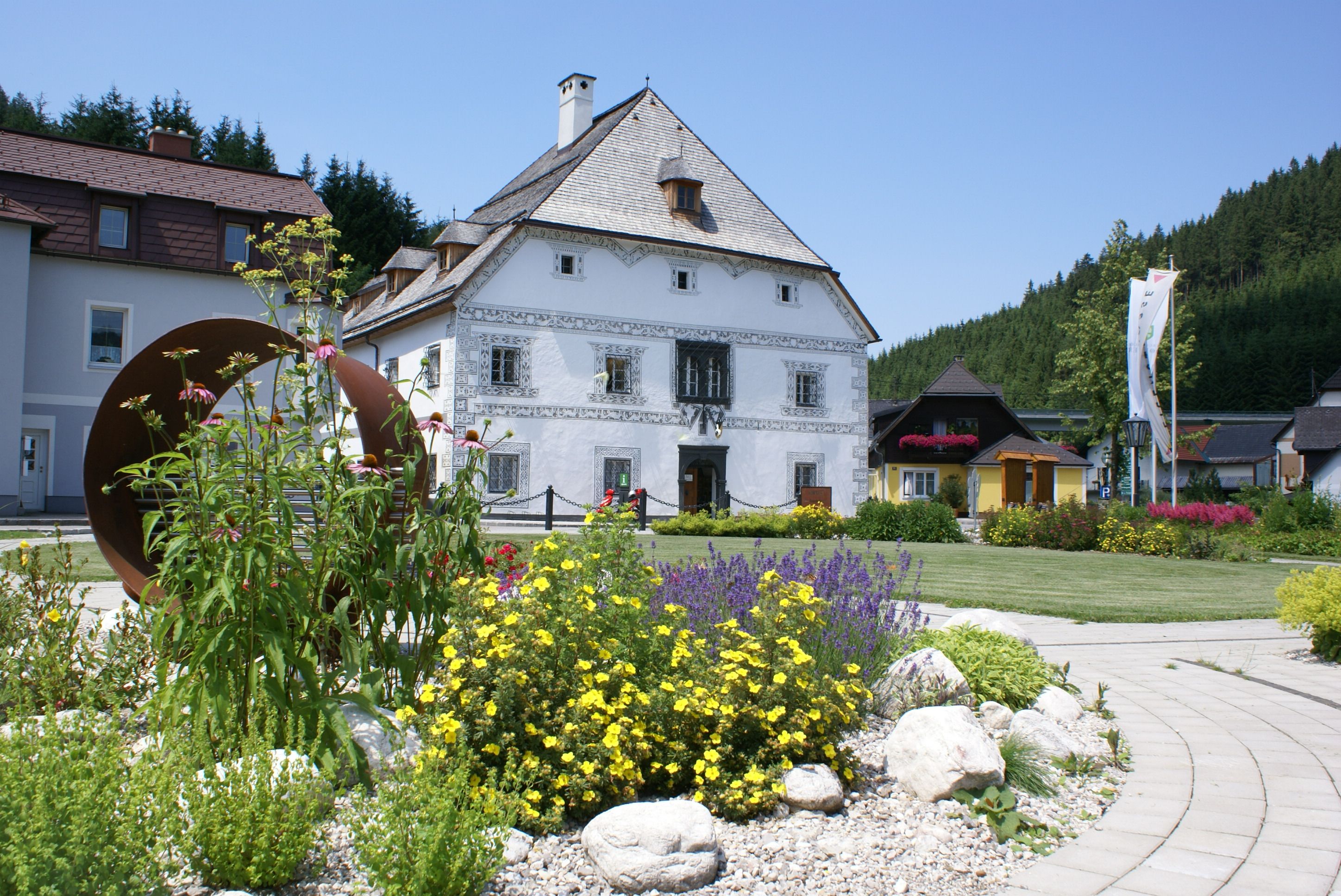 Historic building with ornate gable, surrounded by colorful flowers and a modern work of art in the foreground.