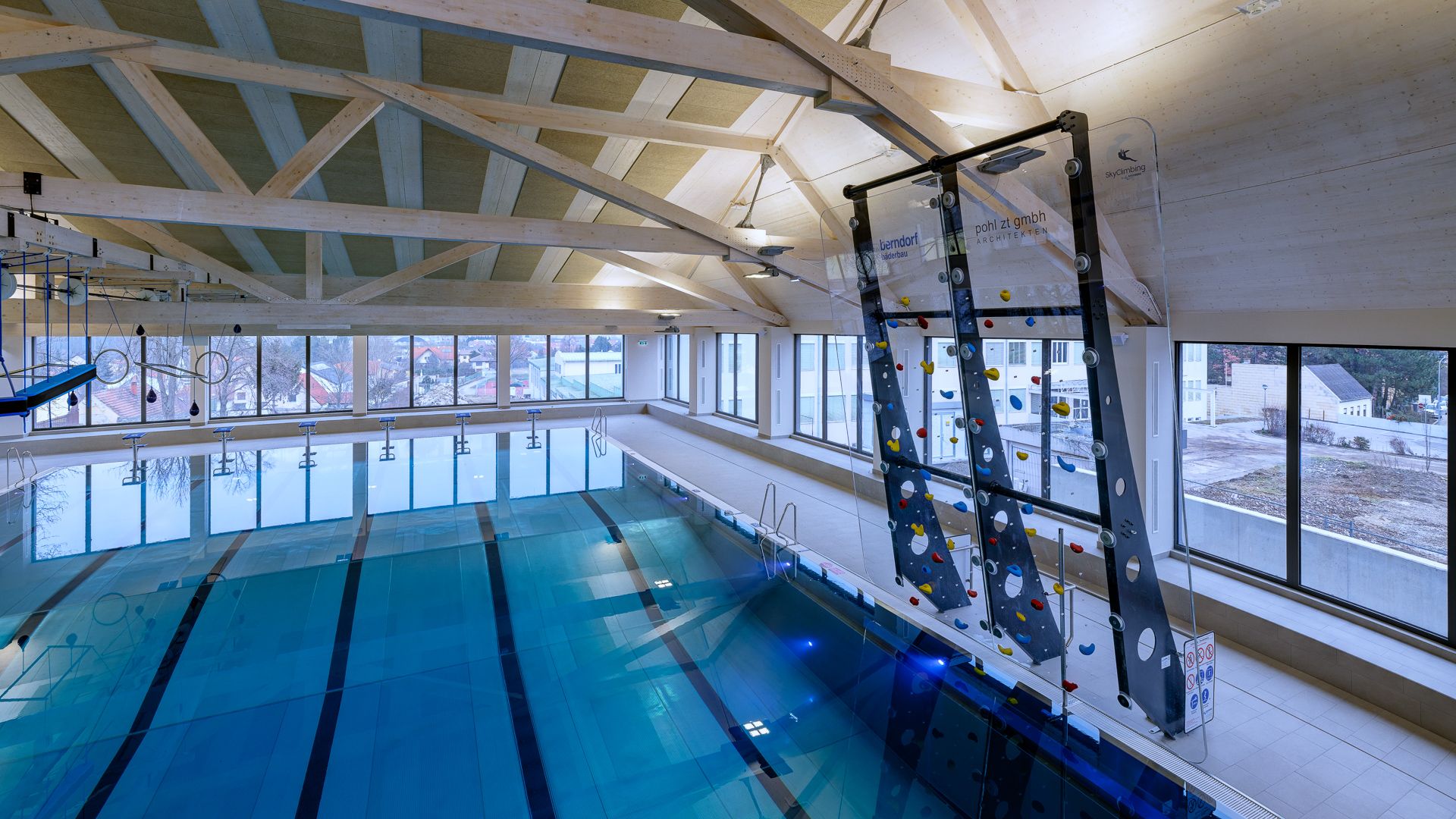 Interior view of a swimming pool with climbing wall and large windows.