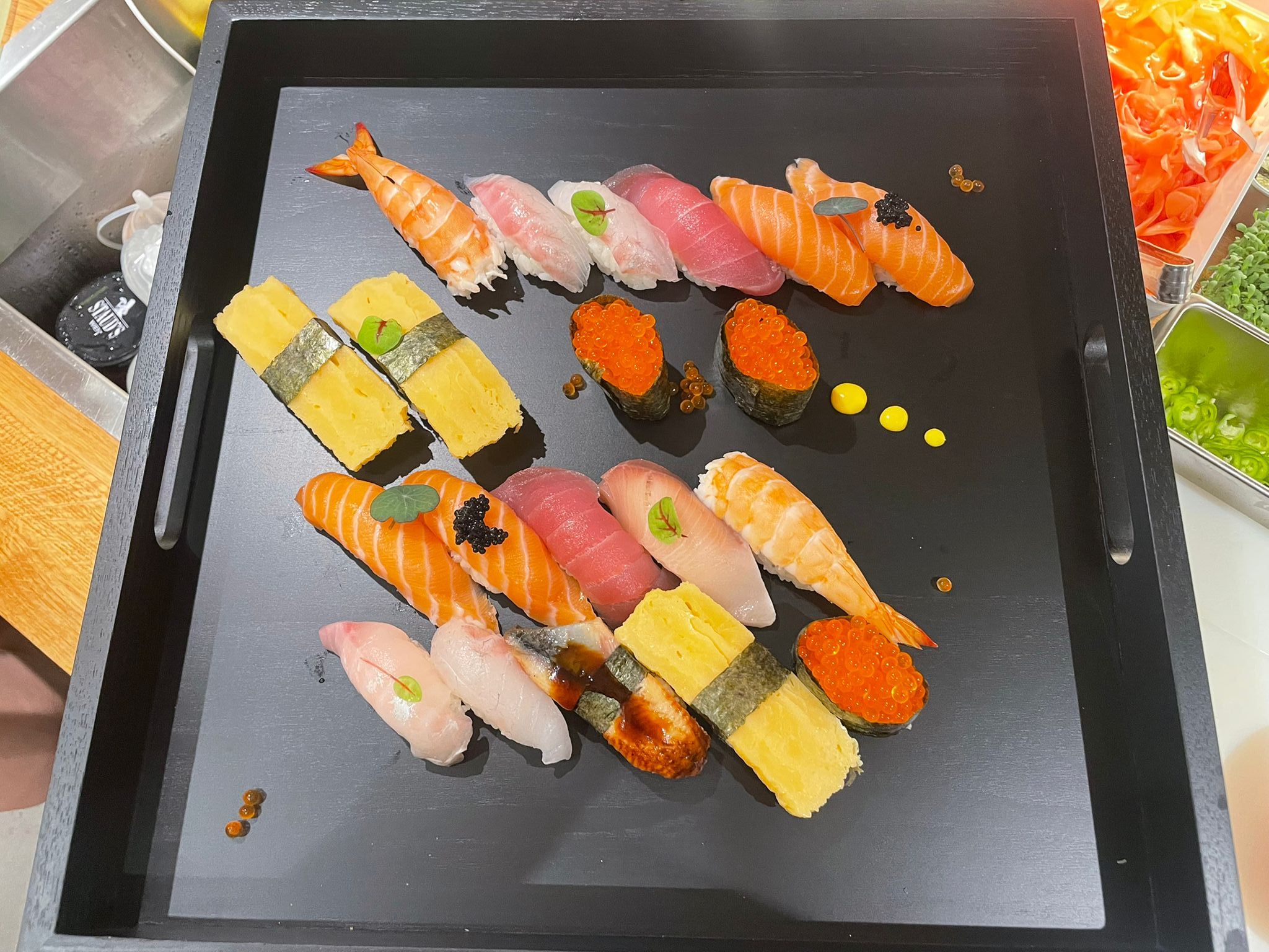 A black tray with a selection of sushi, including nigiri and maki, decorated with caviar and herbs.