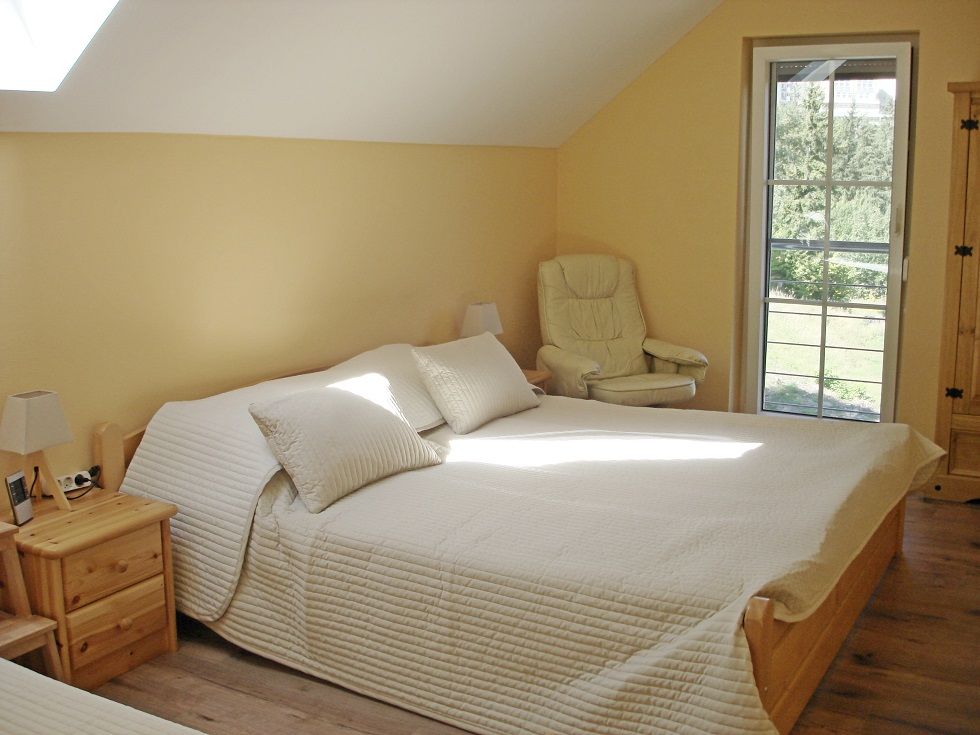 Bright bedroom with double bed, armchair and window with a view of the greenery.