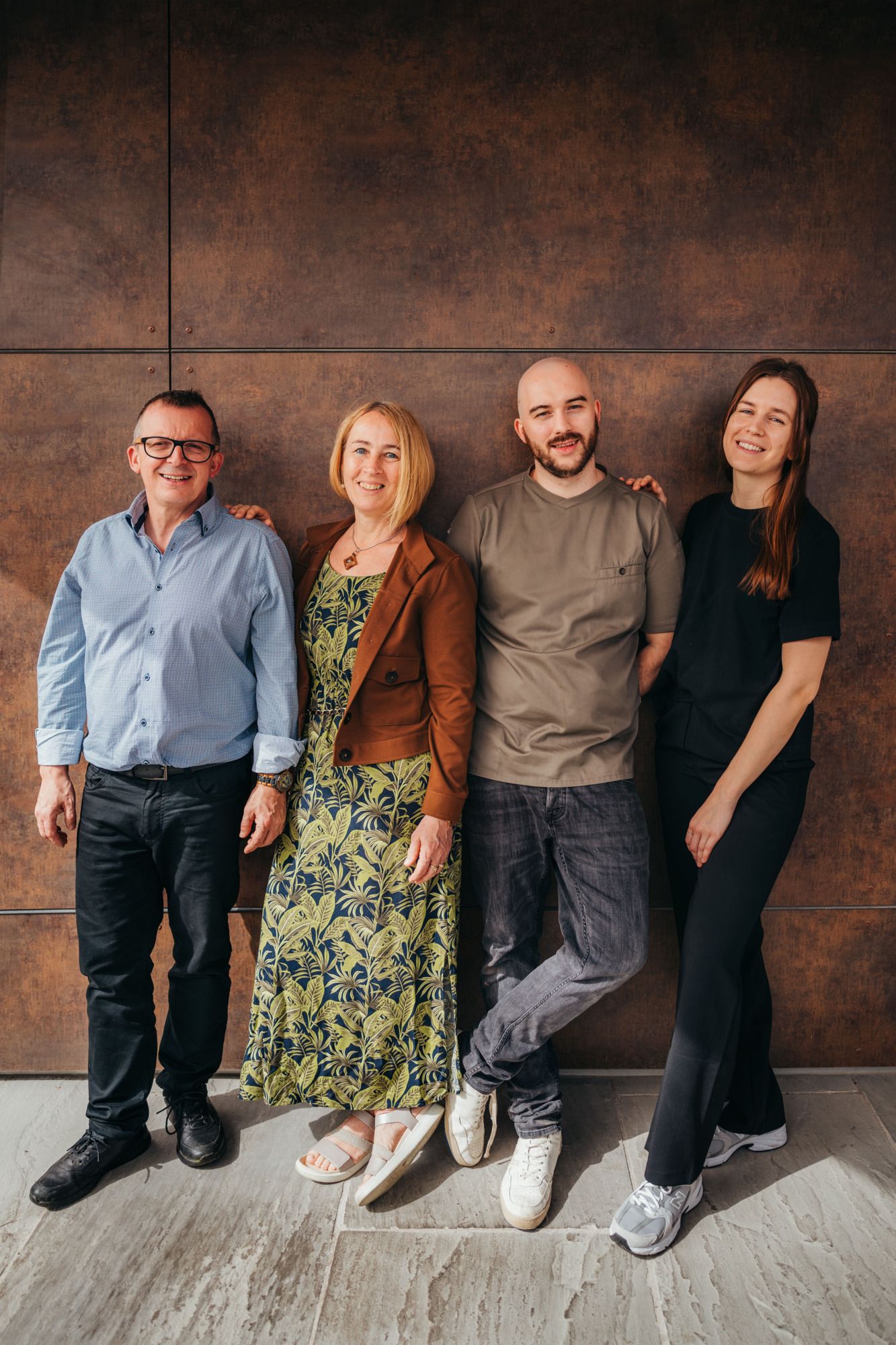 Four people stand smiling next to each other in front of a brown wall.