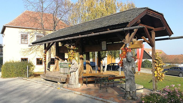 Historic tree press with wooden figures in Droß, surrounded by autumnal vegetation.