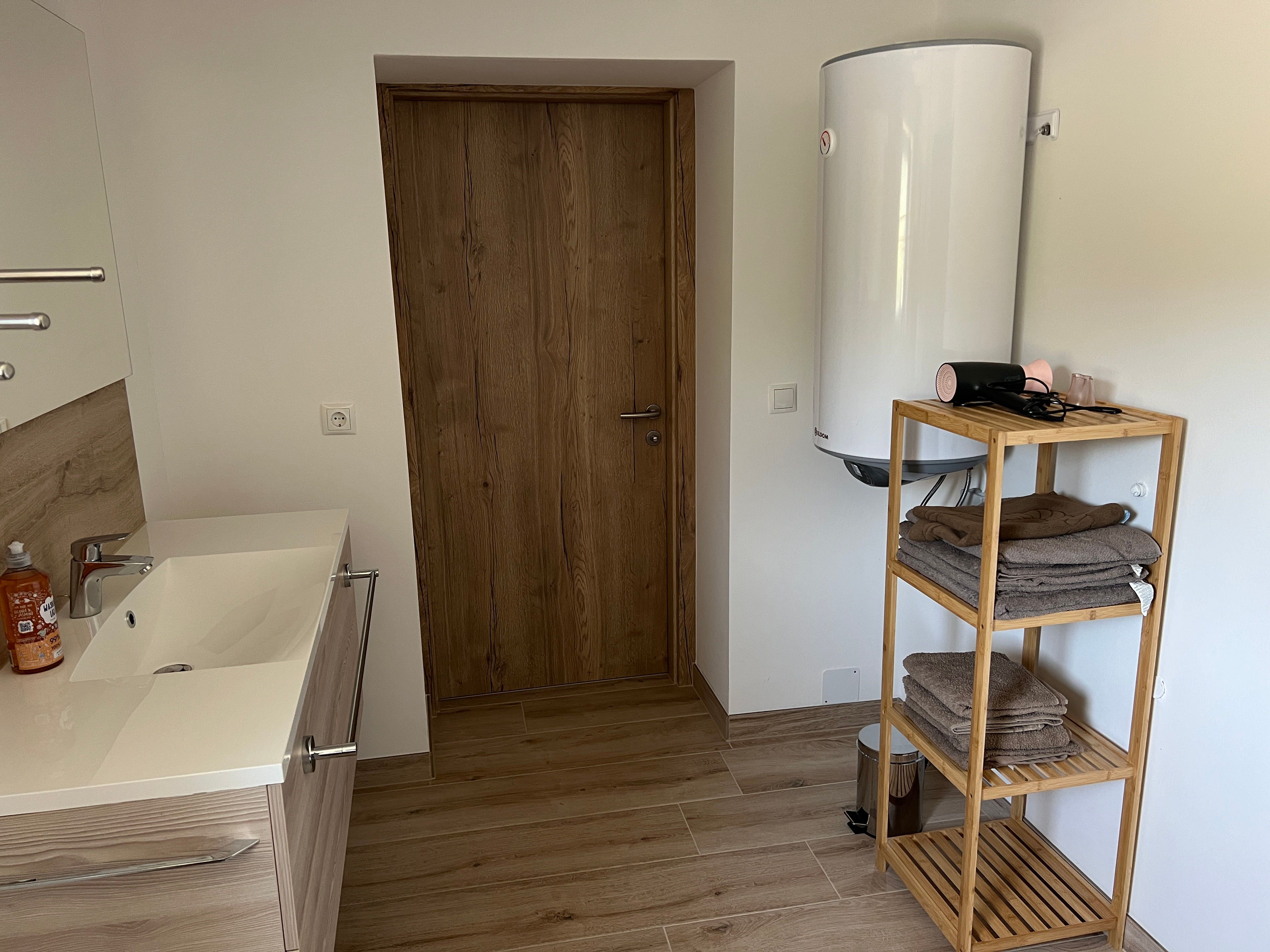 Modern bathroom with wooden shelves, towels, washbasin and hot water boiler.