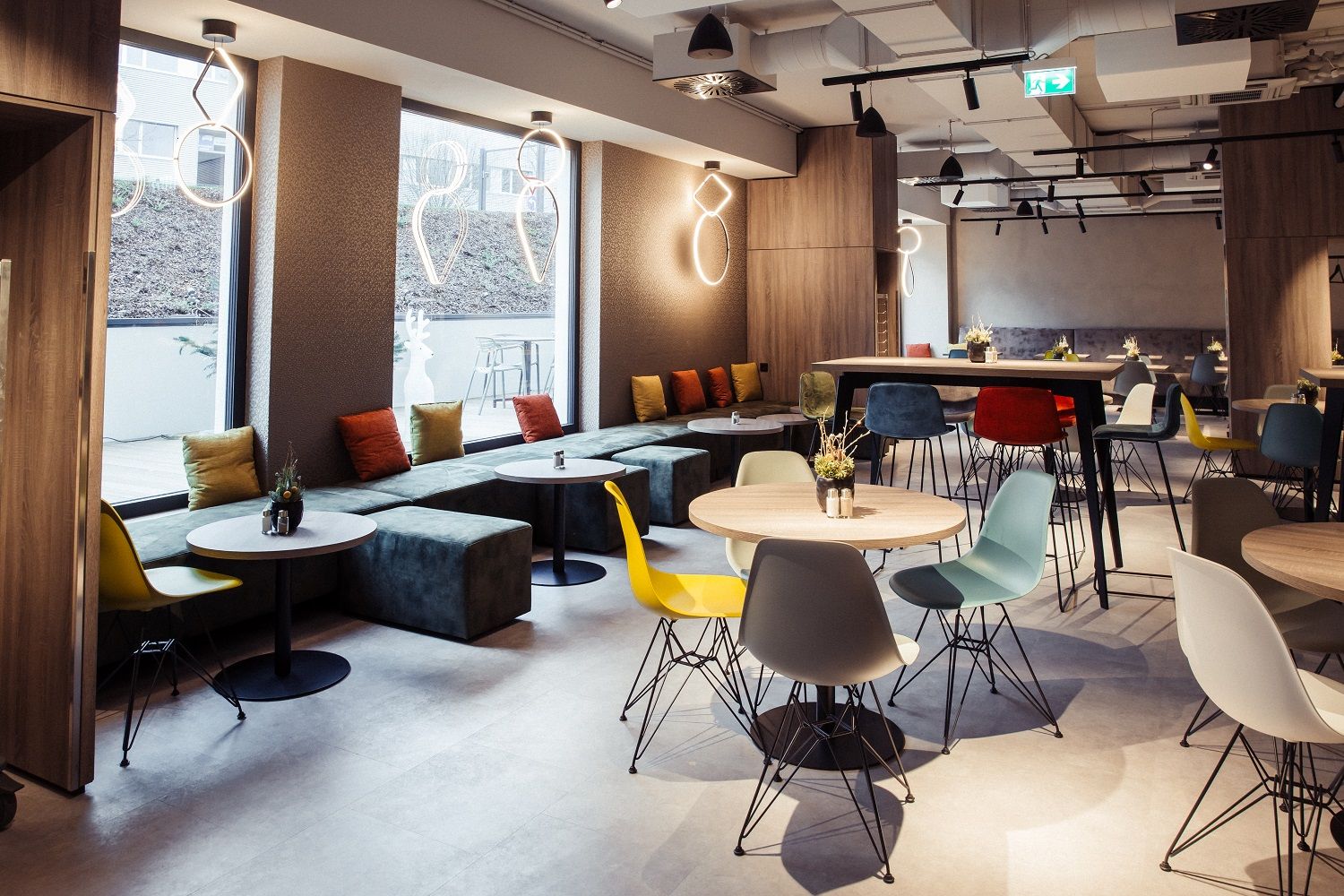 Modern hotel restaurant with colorful chairs and tables, large windows and stylish lighting.