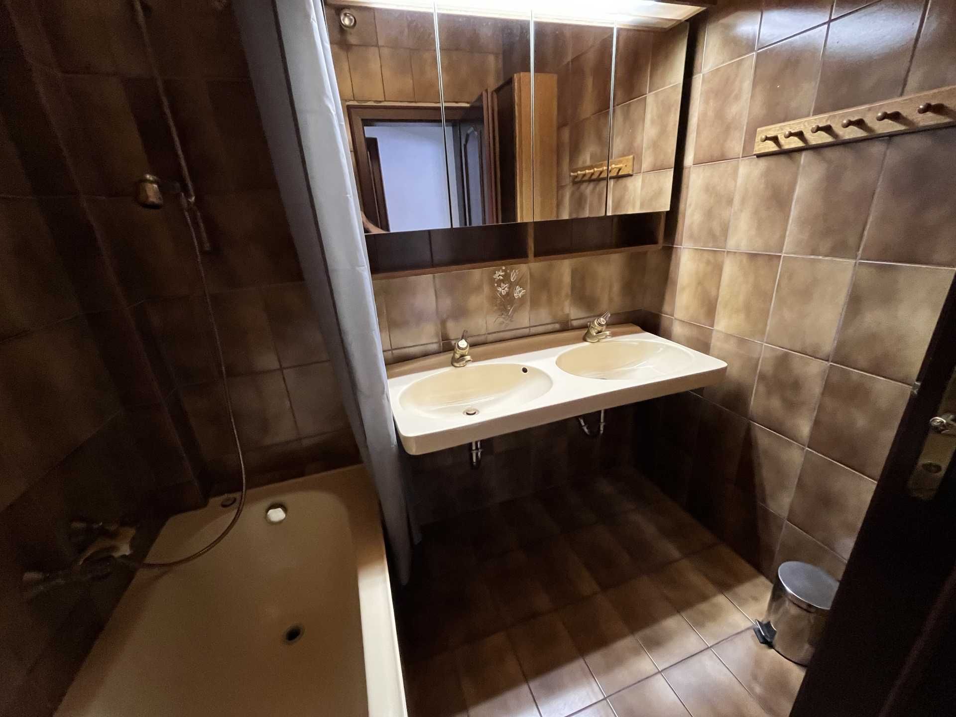 Bathroom with brown tiles, double washbasin, bathtub and mirror.
