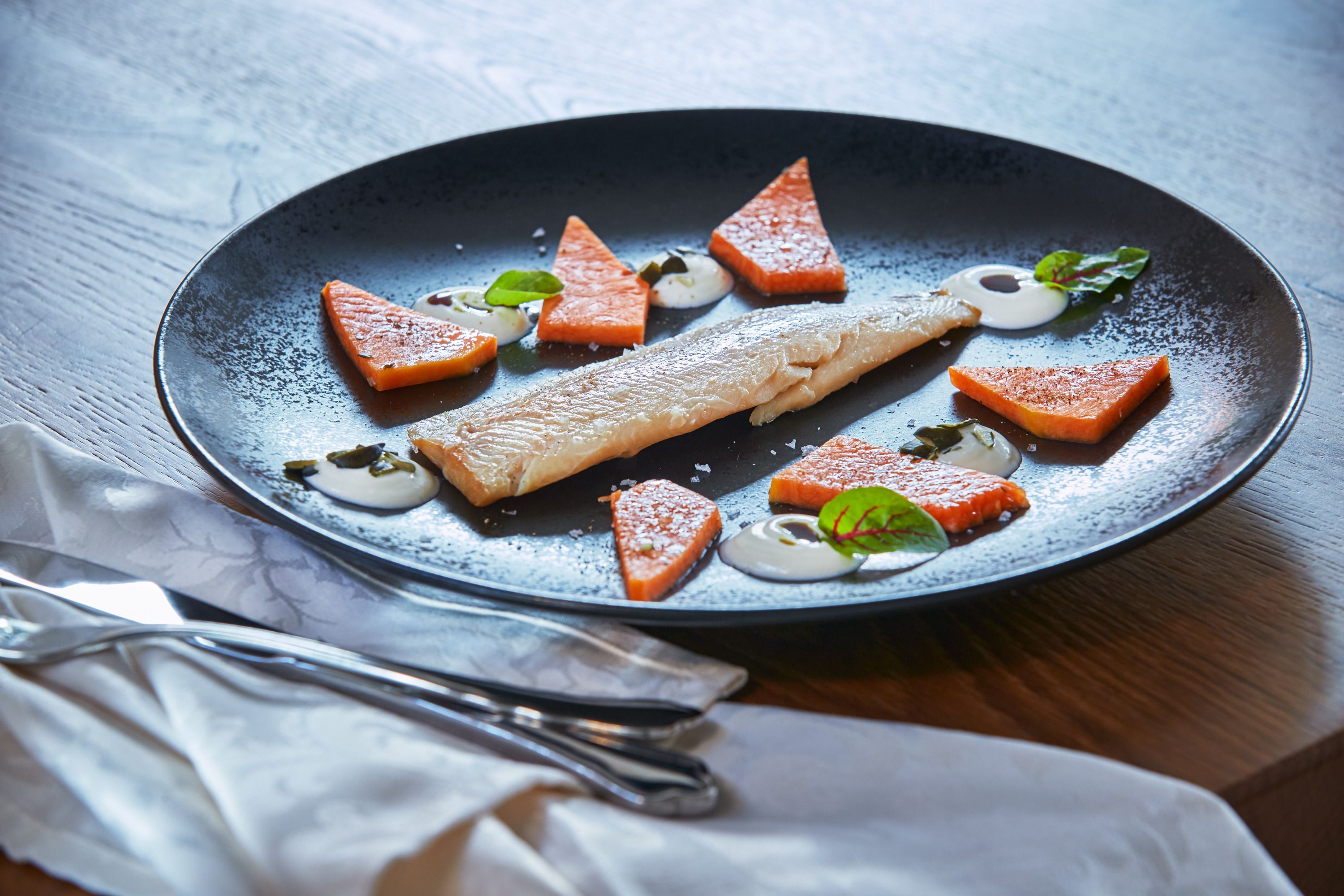 A plate with smoked trout, pieces of pumpkin and sheep's cheese cream, decorated with herbs.