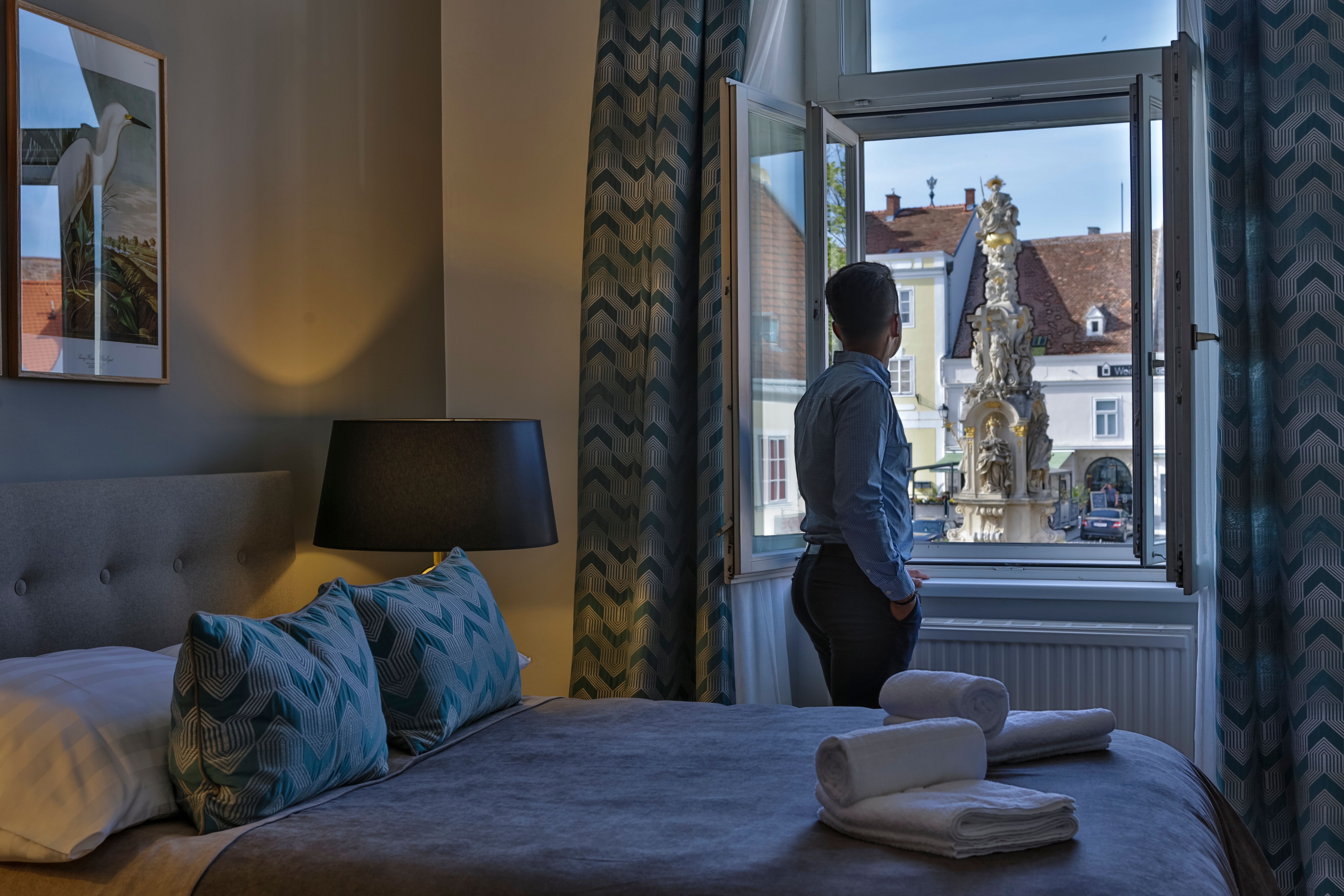 Person stands at the window of a hotel room and looks at a fountain outside.