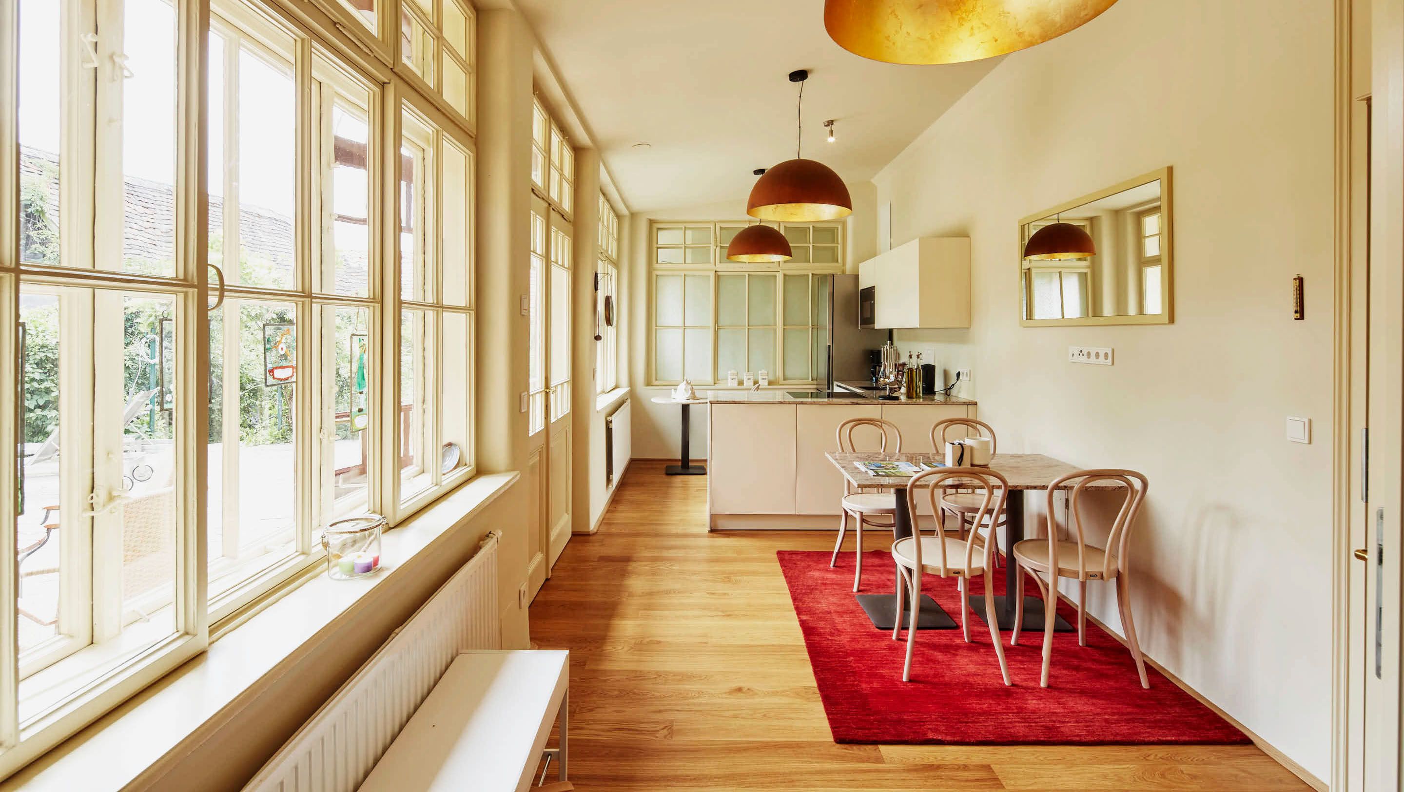 Bright living room with kitchen, wooden floor, red carpet, dining table and large windows.