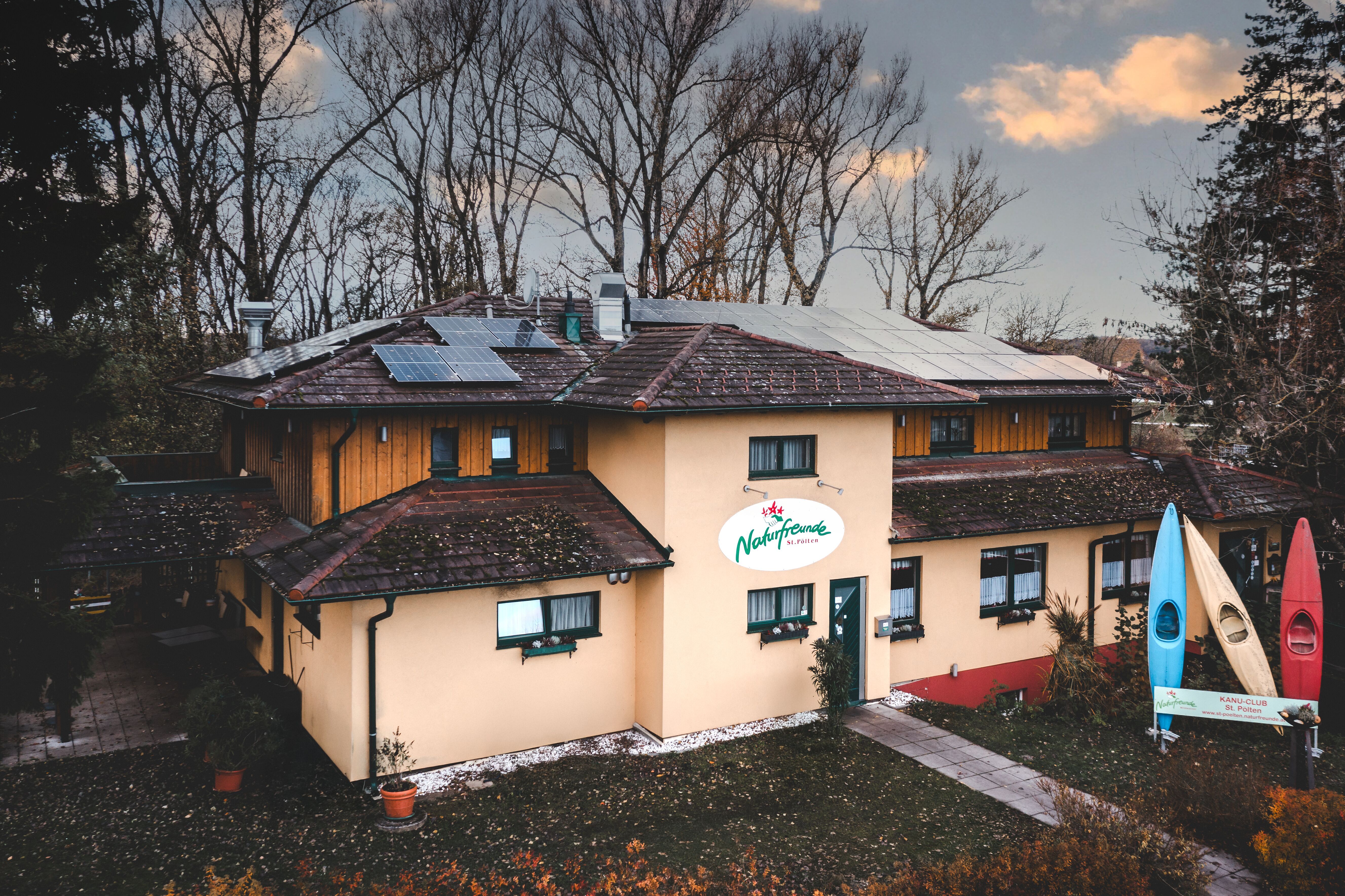 A building with solar panels on the roof and a sign saying 'Friends of Nature'. There are three colorful canoes in front of the building.