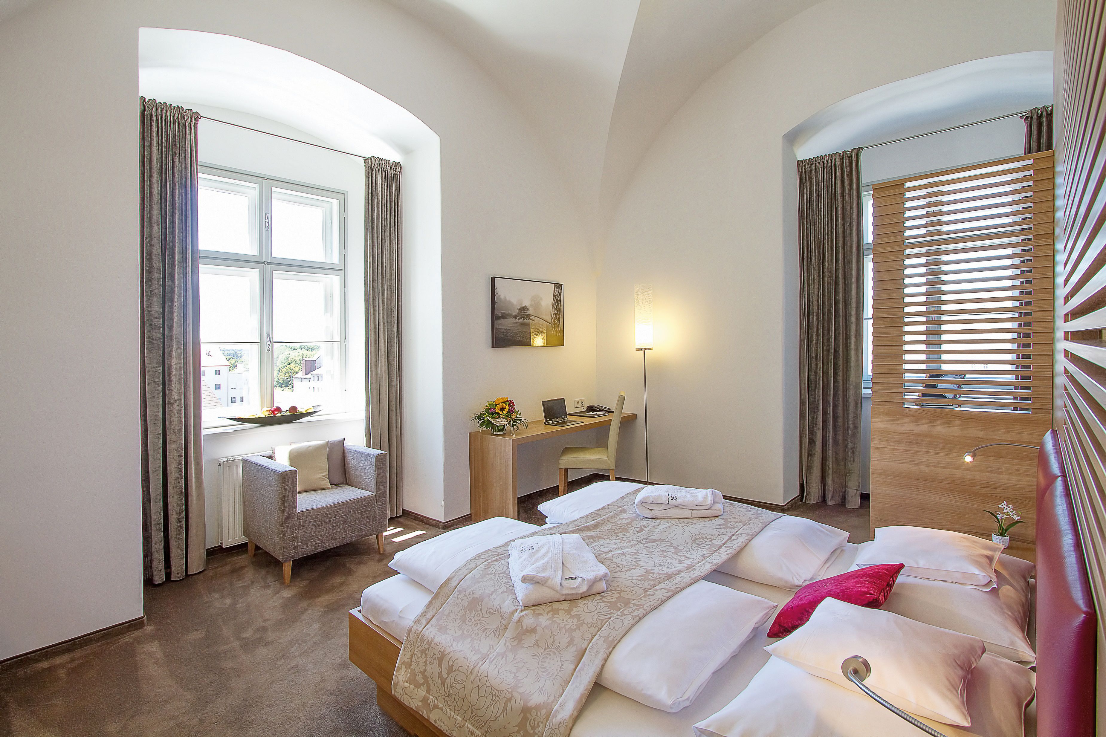 Hotel room with double bed, desk, armchair and large window.