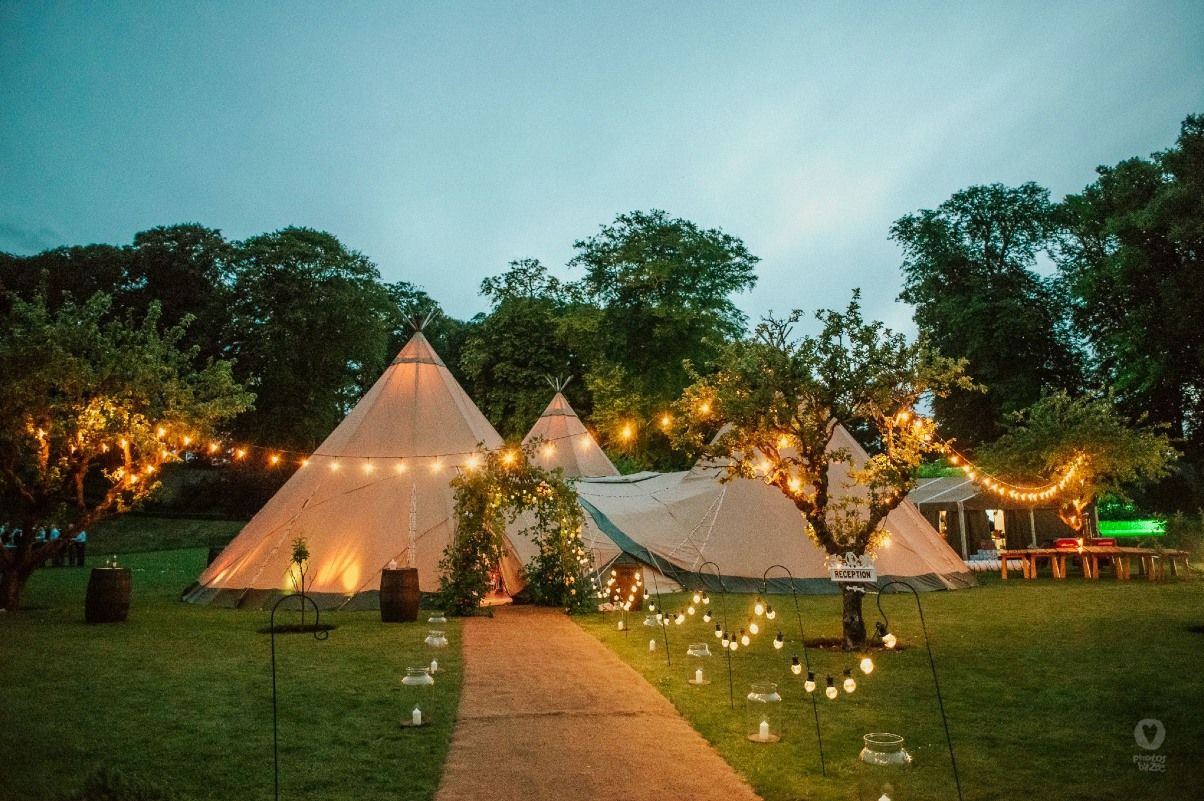 An illuminated teepee tent in a garden with fairy lights and trees at dusk.