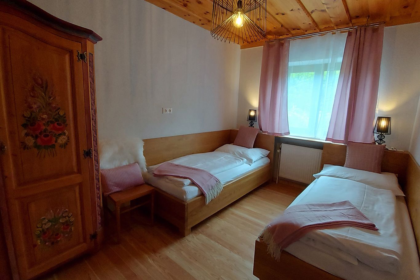 Cozy bedroom with two single beds, wooden furniture and pink curtains.