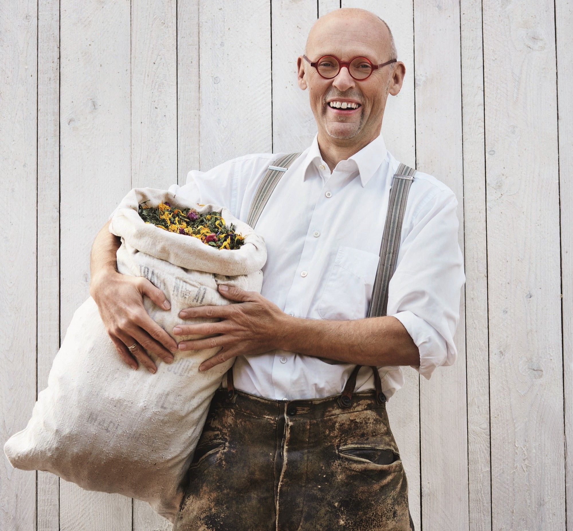 Johannes Gutmann, founder of SONNENTOR, holds a bag full of herbs in front of a wooden wall.