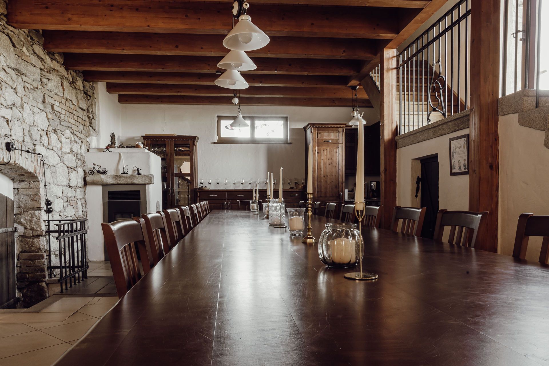 Large room with long wooden table, wood-burning stove and stone wall.
