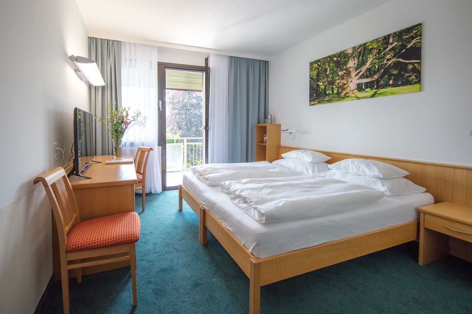 Hotel room with double bed, desk, chair and balcony.