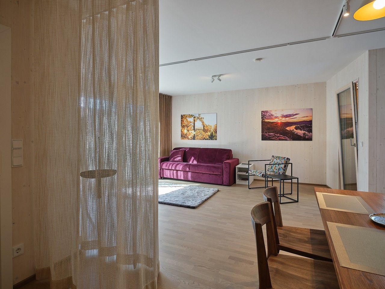 Living room with purple sofa, wooden table and chairs, curtain, and murals.