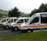 Four white vans with yellow and red stripes are parked next to each other in a parking lot.