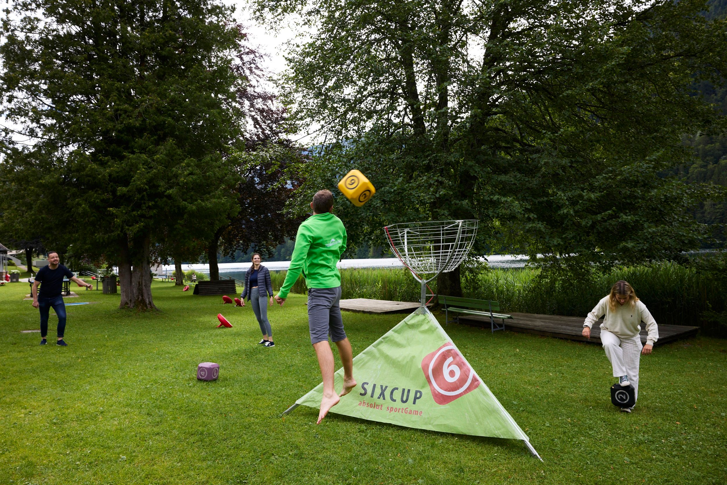 People play an outdoor throwing game with large dice on a meadow.