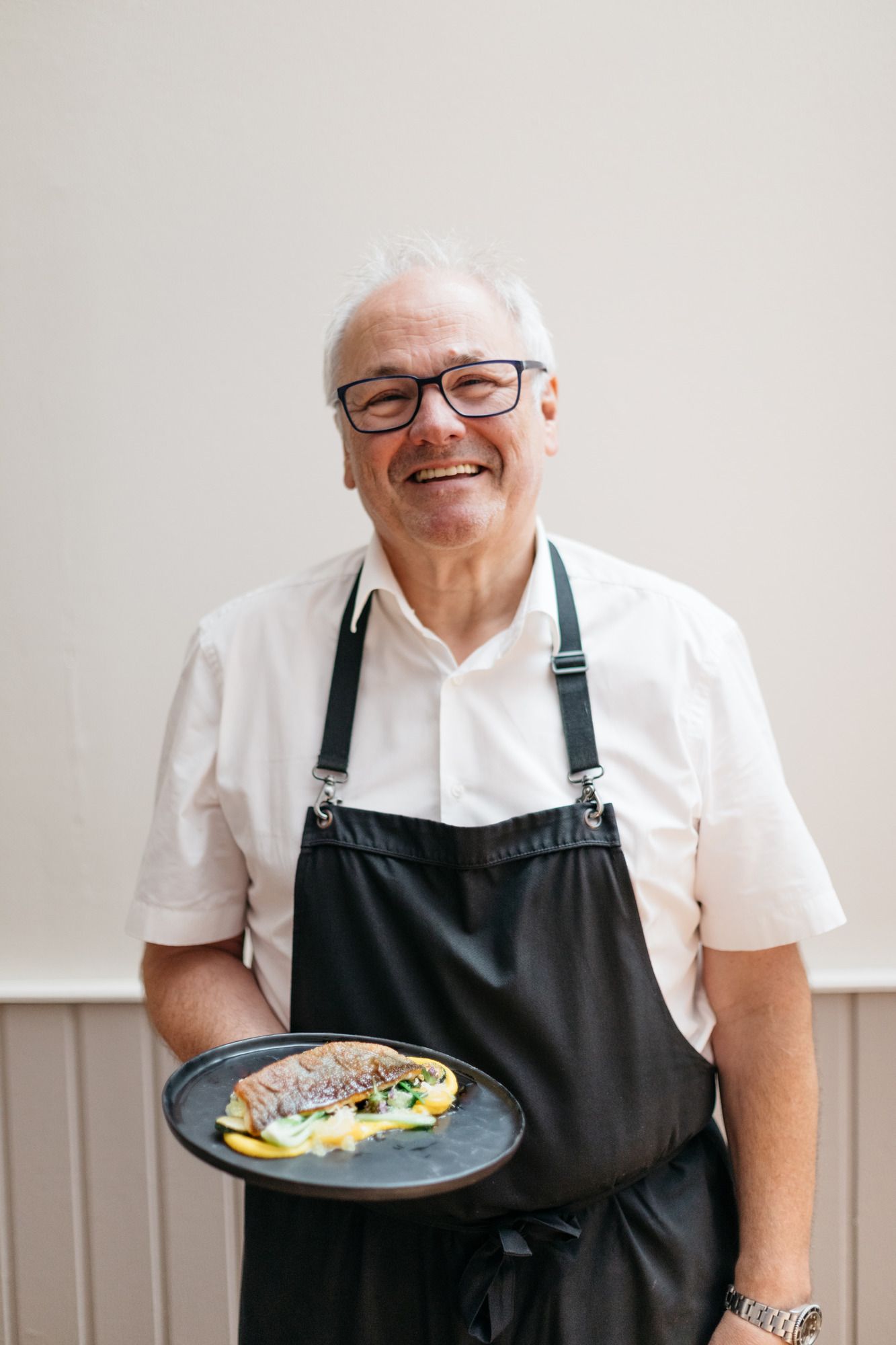 A smiling man in an apron holds a plate of food.