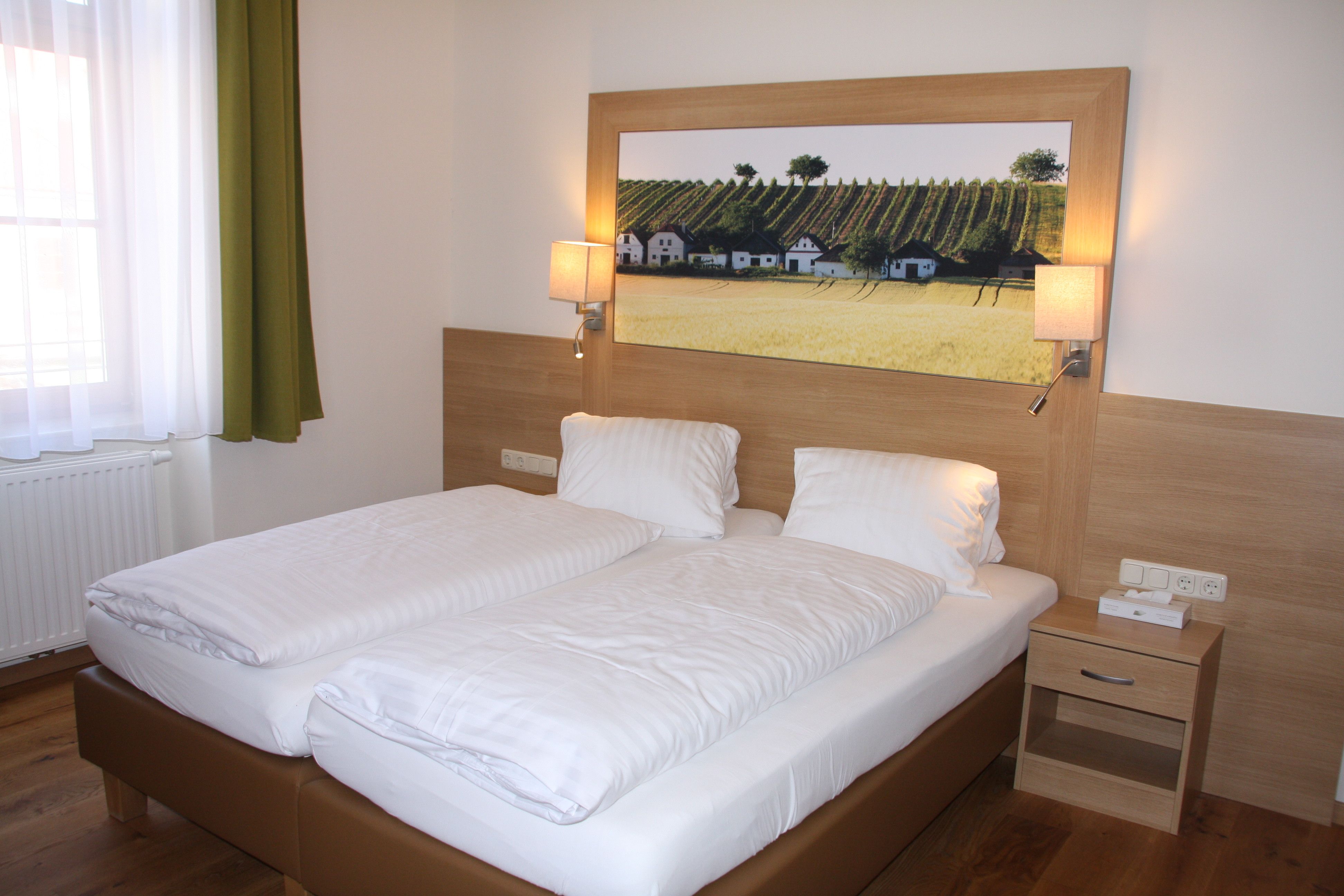 A guest room with a double bed, wooden paneling, bedside table and a picture of vineyards on the wall.