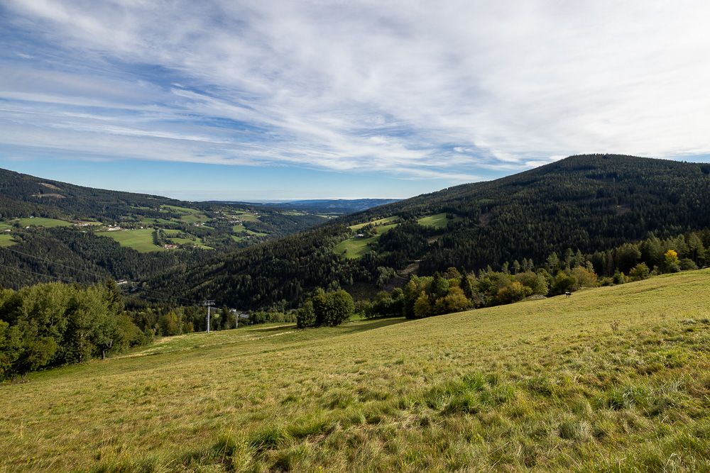 Vast green landscape with hills and forests under a cloudy sky.