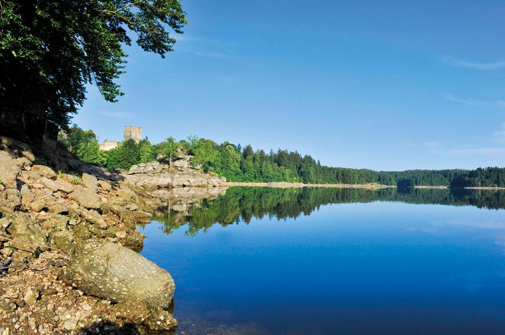 Kampsee Ottenstein with calm water, wooded shores and a castle in the background.