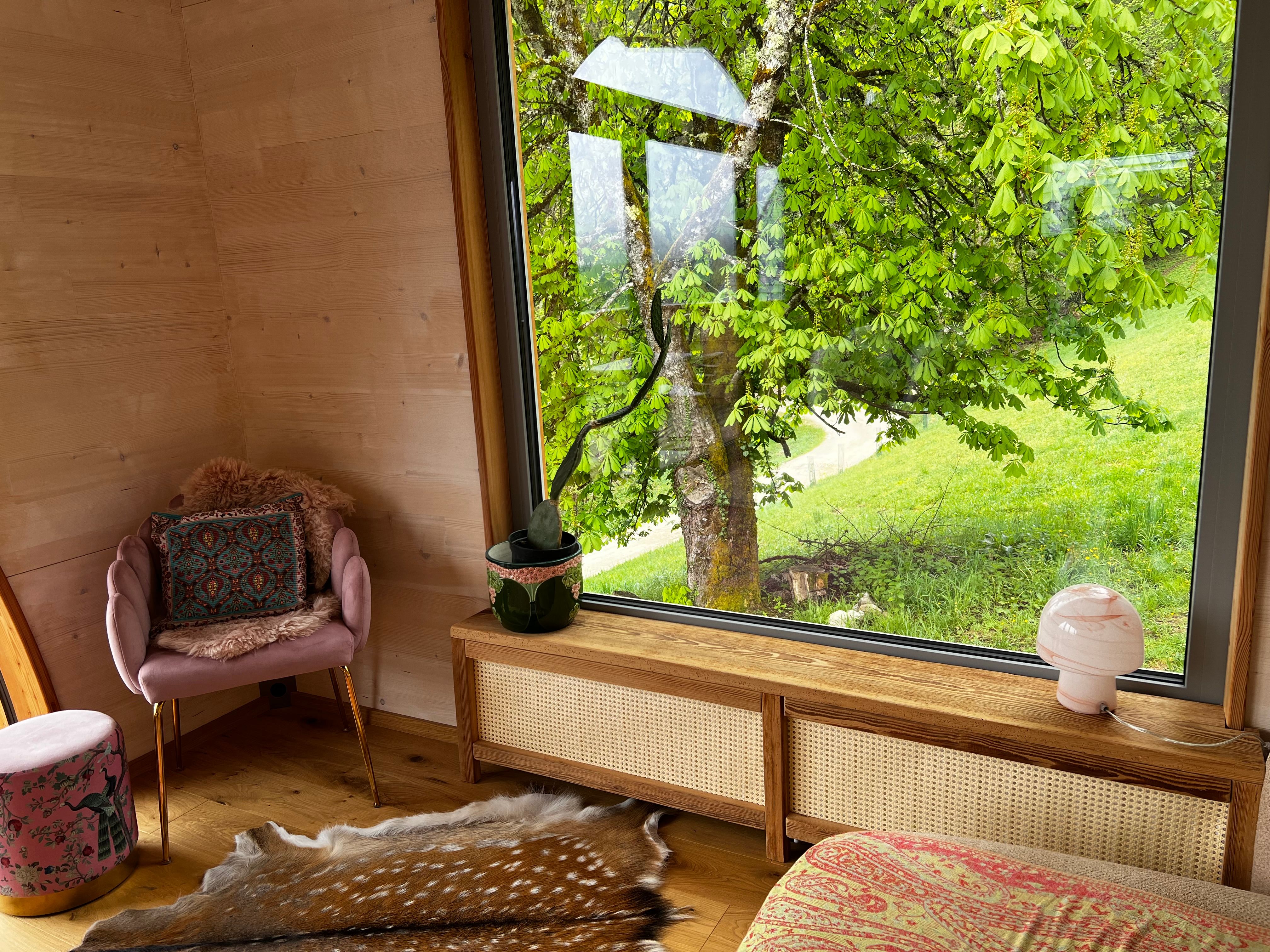 Interior of a cozy room with large window and view of a tree and green meadow.