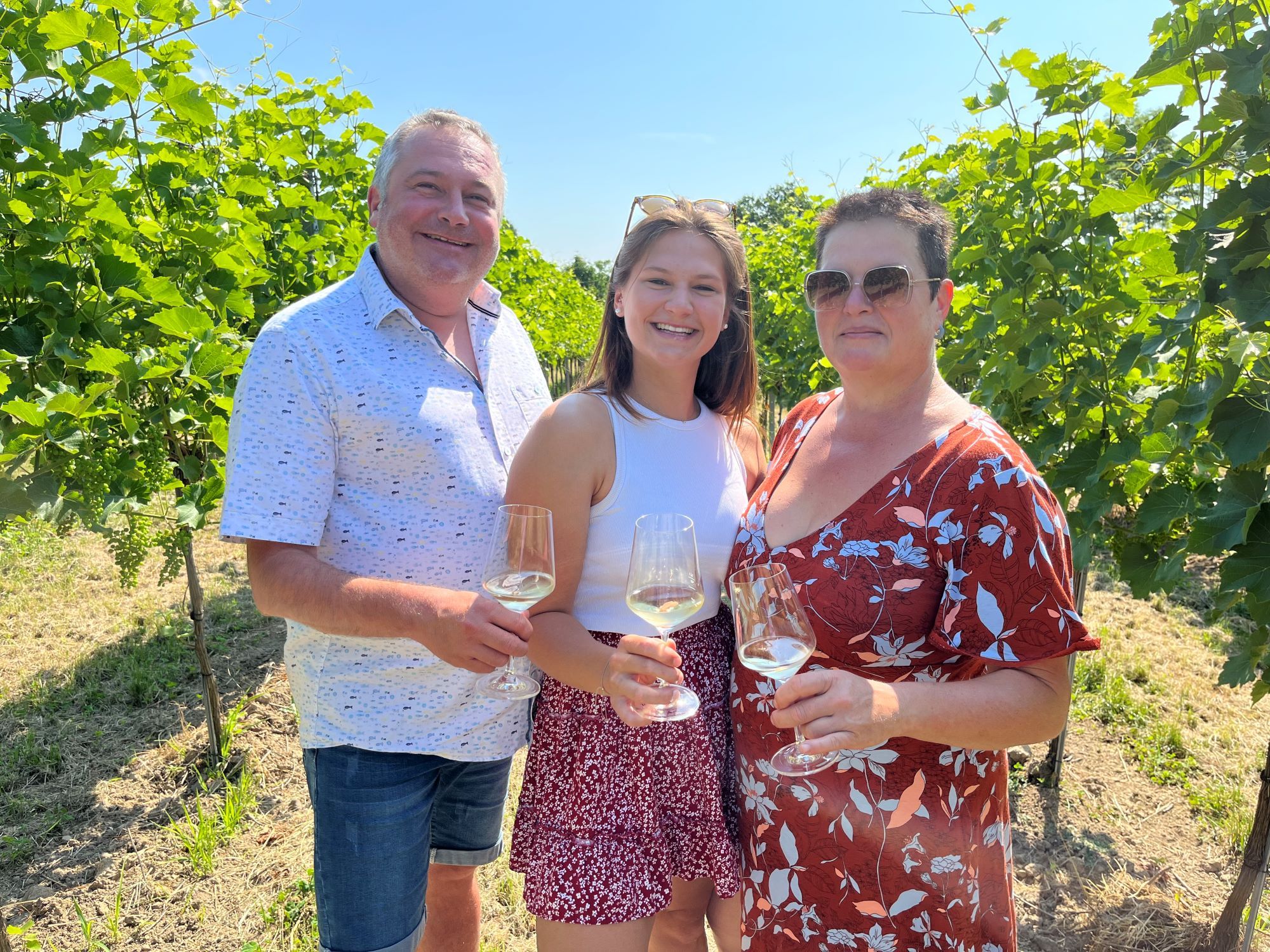 The Heimel family with wine glasses in hand. The family stands between vines. 