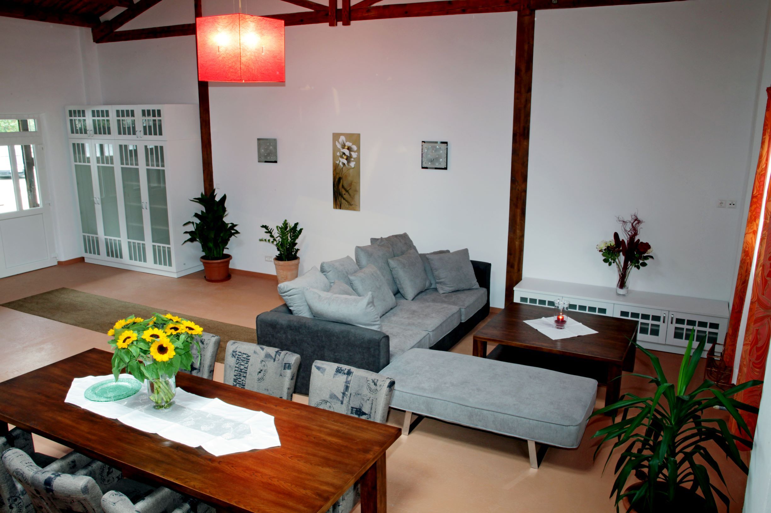 A modern loft with a gray sofa, dining table with sunflowers, plants and a red lampshade.