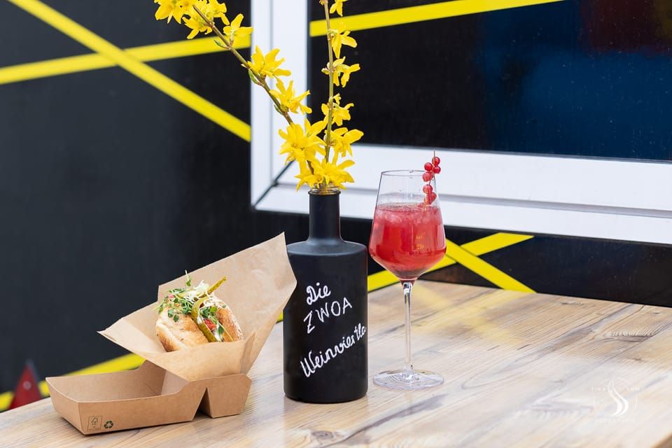 A drink and a sandwich on a table with a vase of yellow flowers.