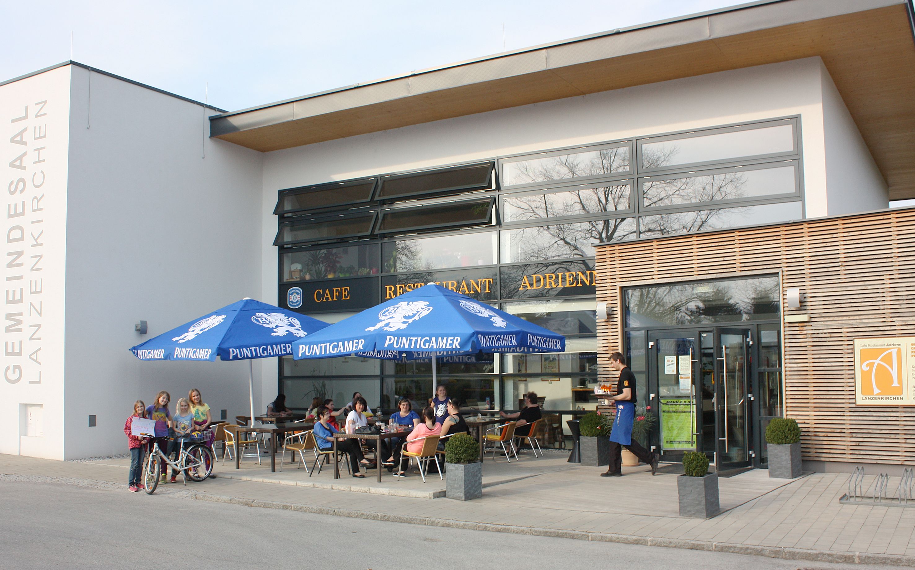 Exterior view of Cafe Adrienn with guests under blue parasols.