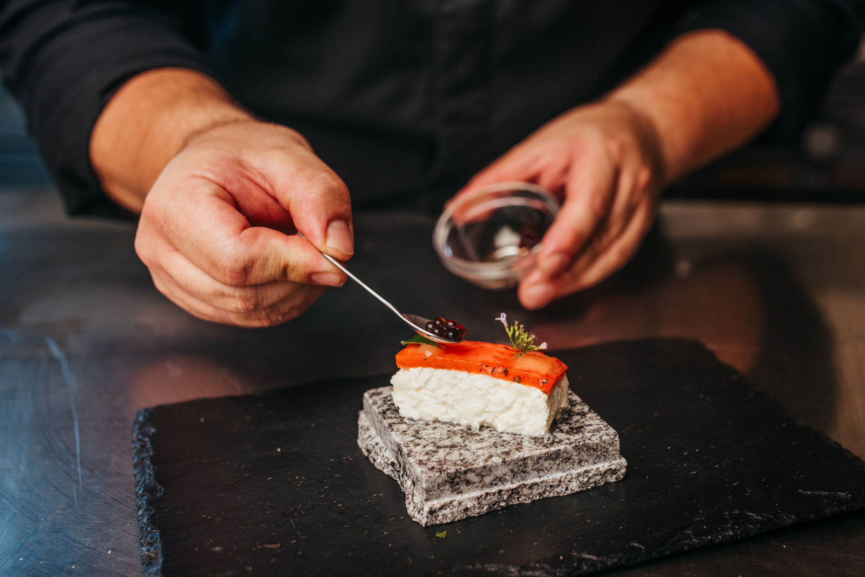A chef decorates a piece of sushi with caviar on a stone.