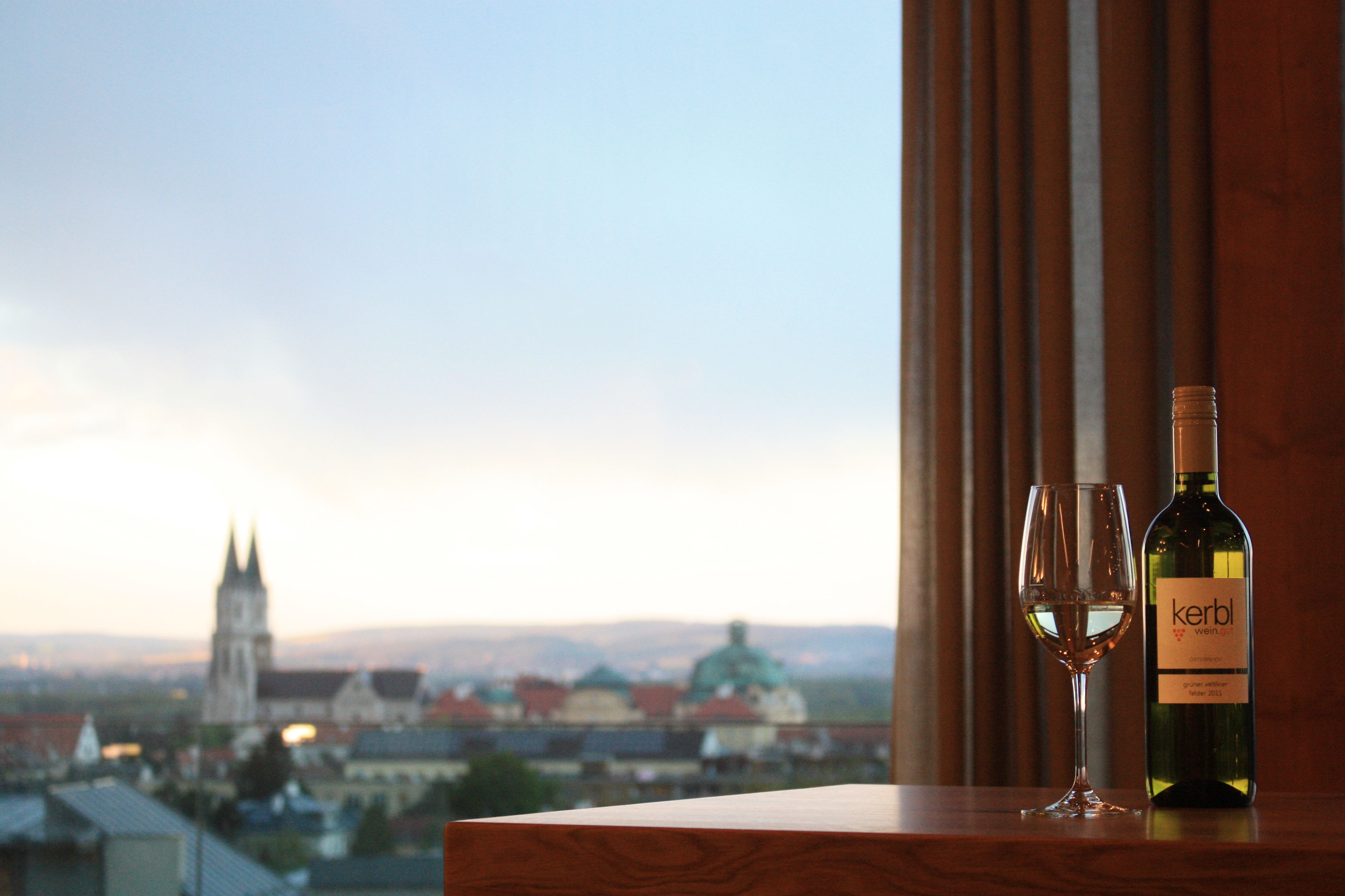 Wine bottle and glass in front of city panorama with church.