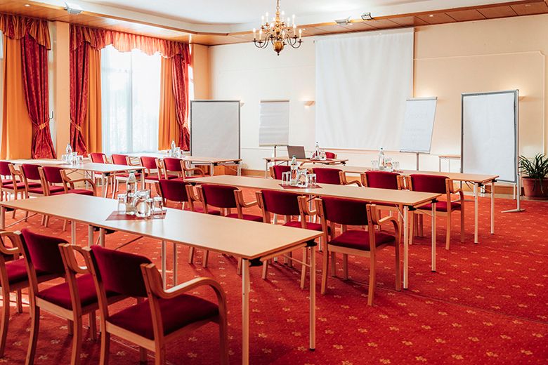 A seminar room with red chairs, tables, flipcharts and a projector.