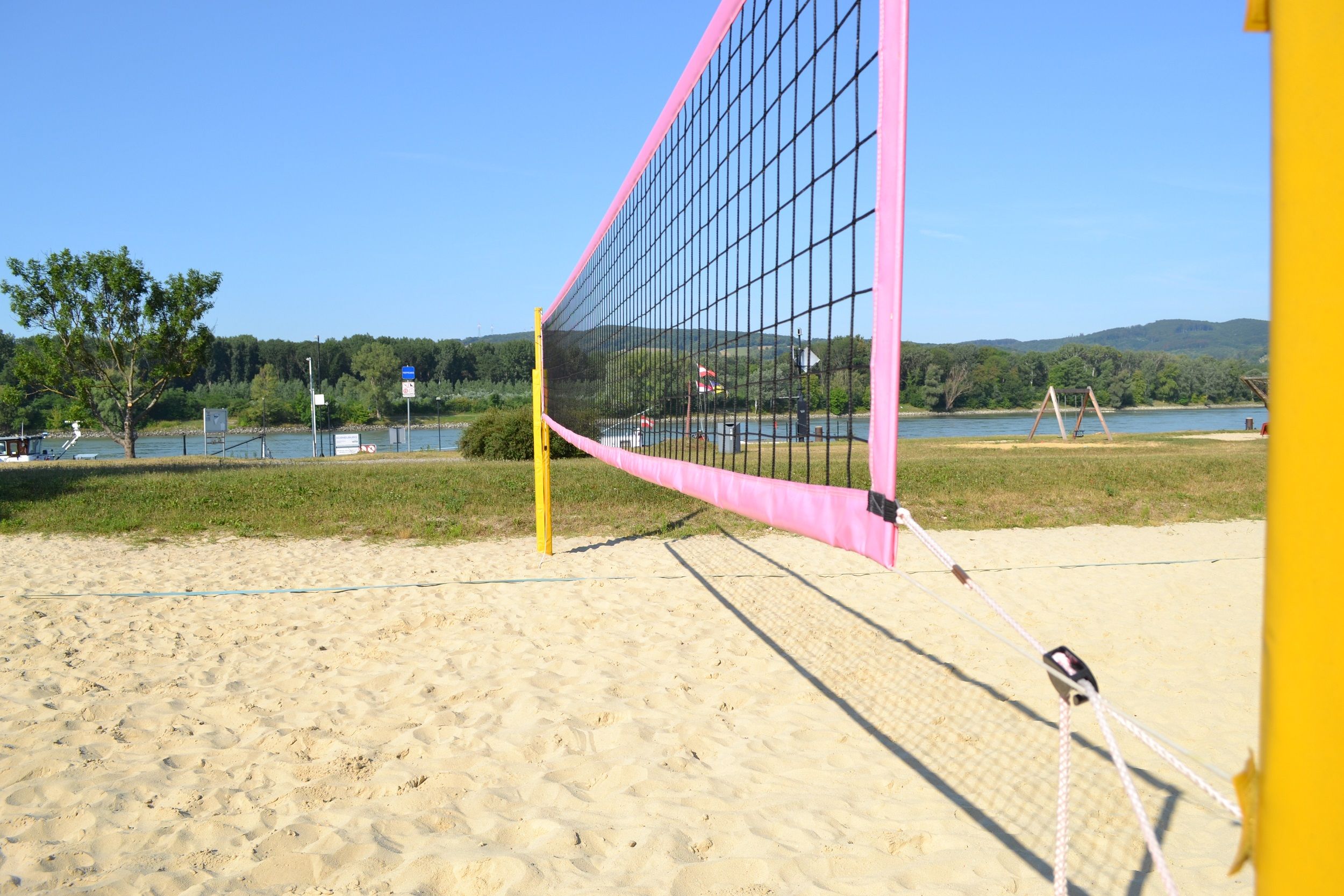 Beach volleyball court with net, sand and river in the background.