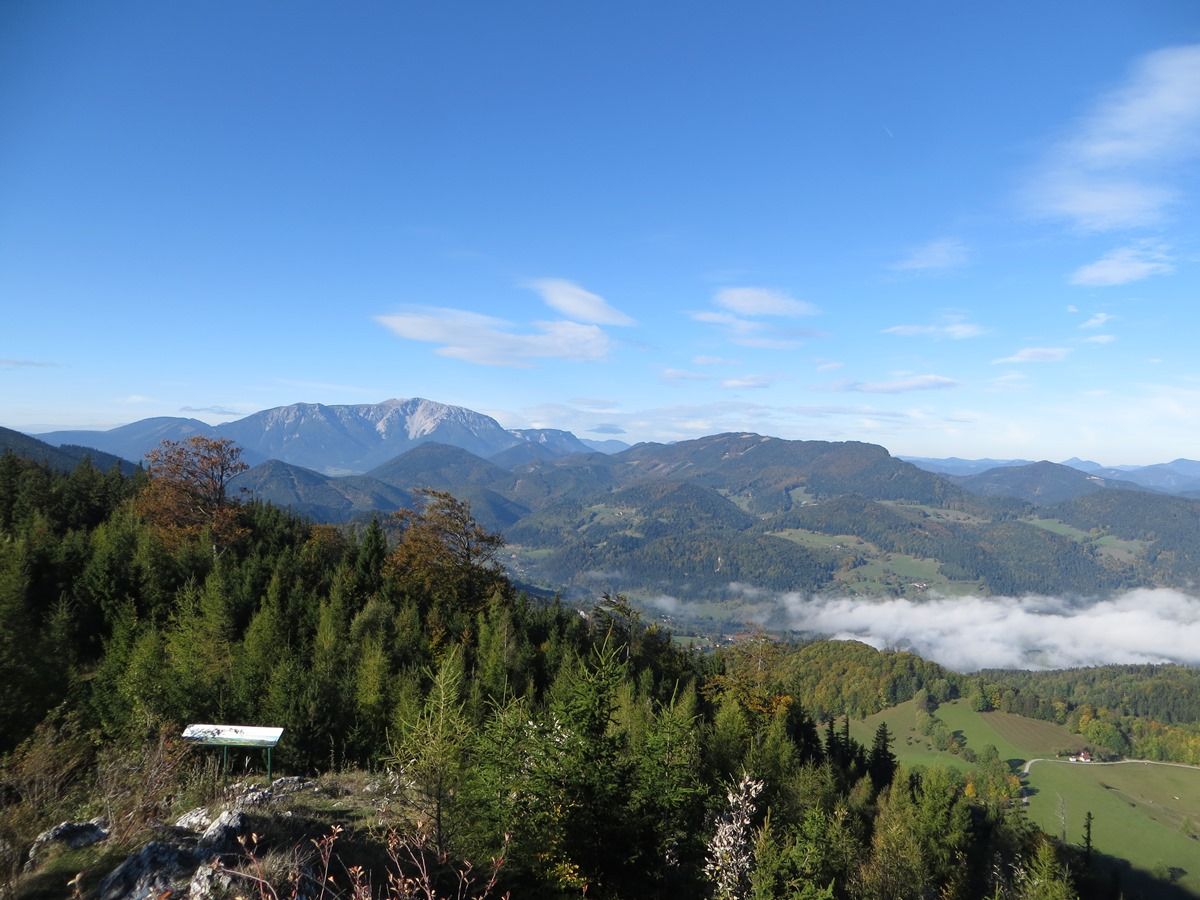 Panoramic view of wooded hills and mountains under a blue sky with scattered clouds.