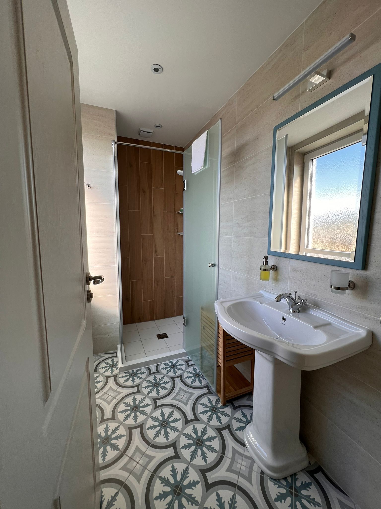Modern bathroom with patterned tiled floor, washbasin, mirror and shower with glass wall.
