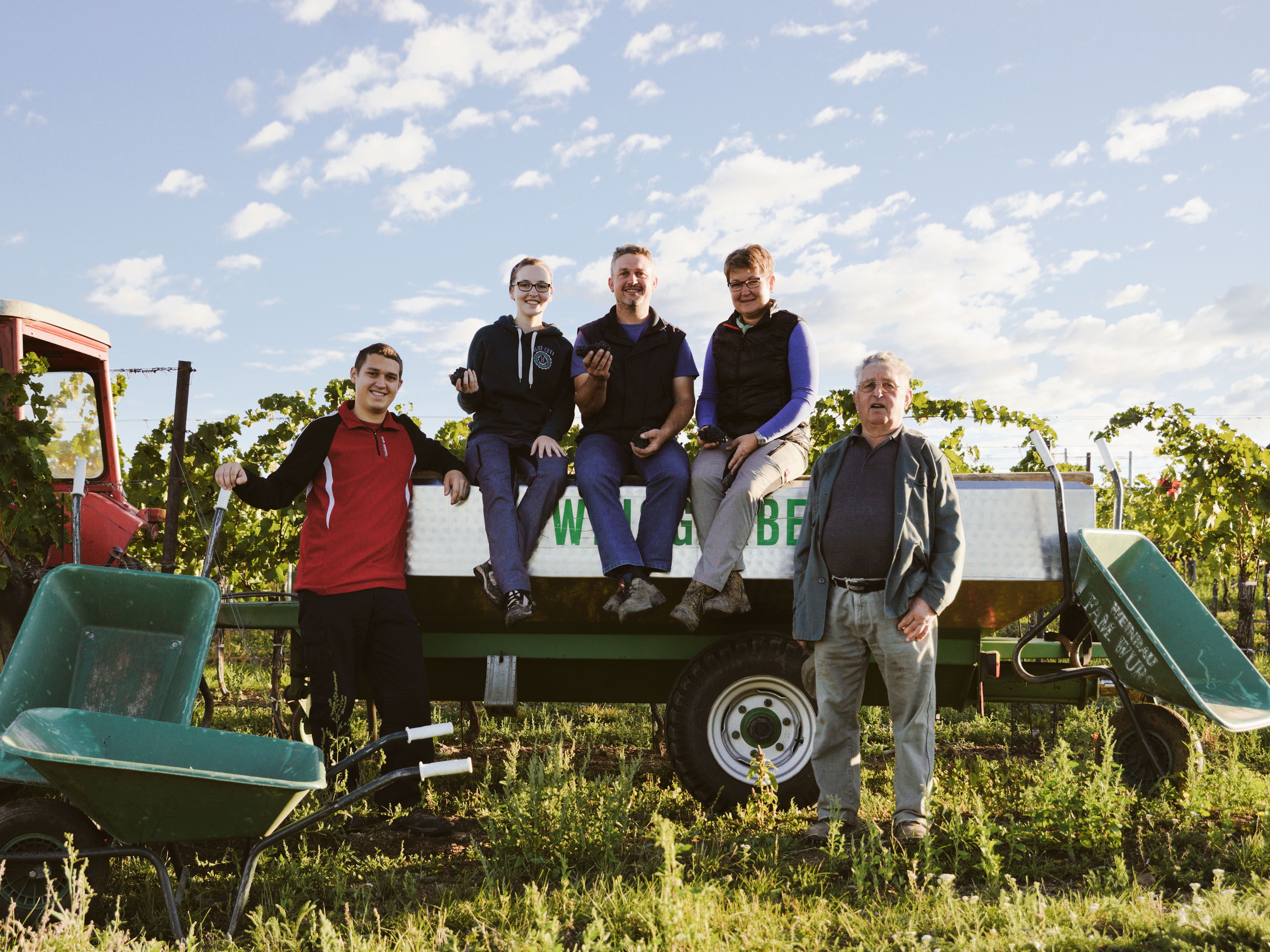 A family poses on a tractor trailer in a vineyard.