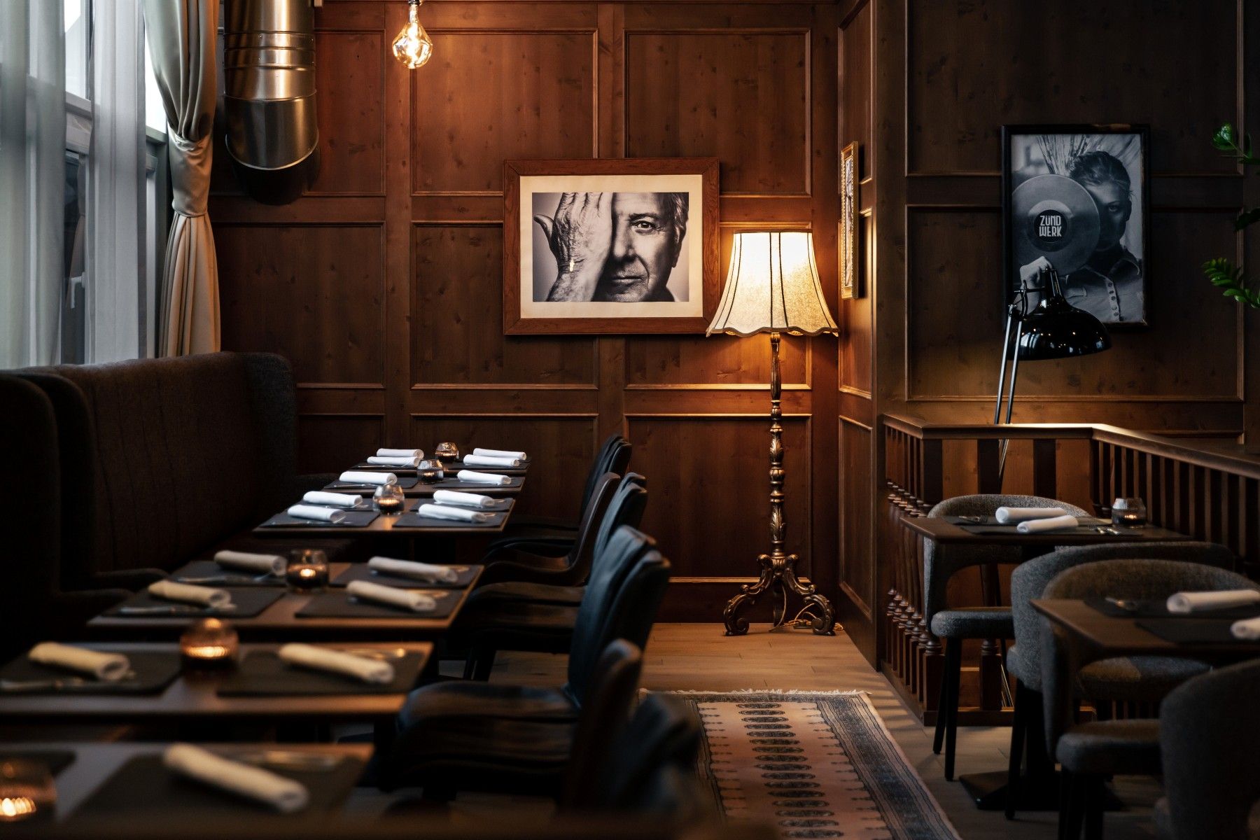 Cozy room with wooden walls, set tables, floor lamp and black and white photographs on the wall.