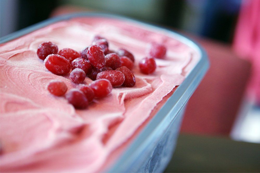 Pink ice cream with red berries in a metal tub.
