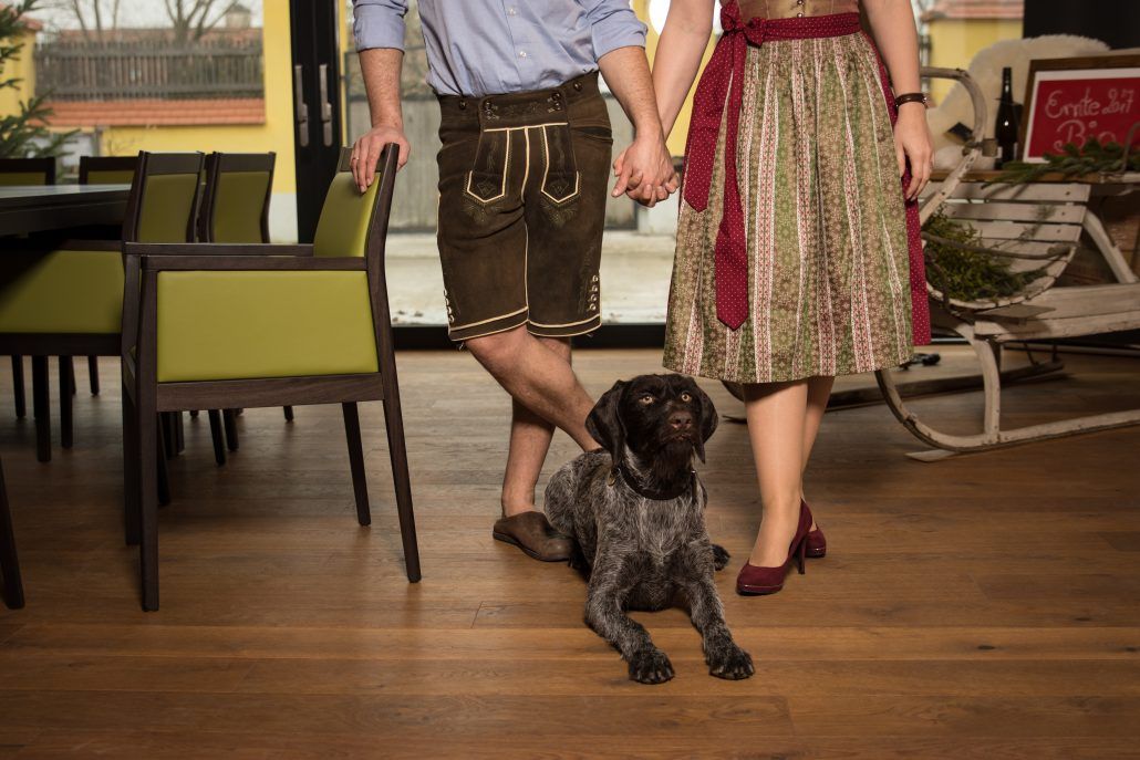 A couple in traditional dress hold hands, a dog sits at their feet.
