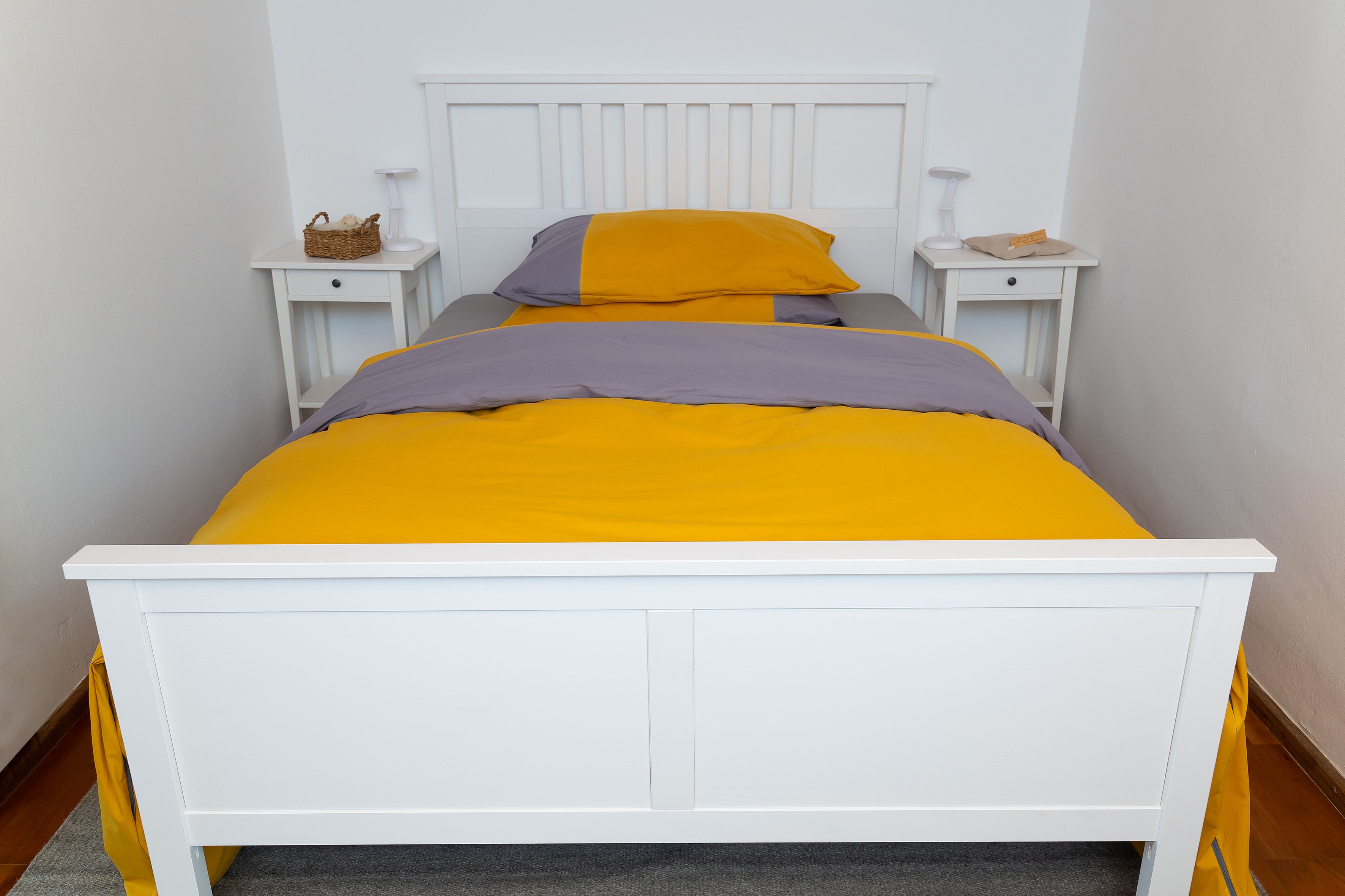 A white bed with yellow-grey bed linen in a plain bedroom.