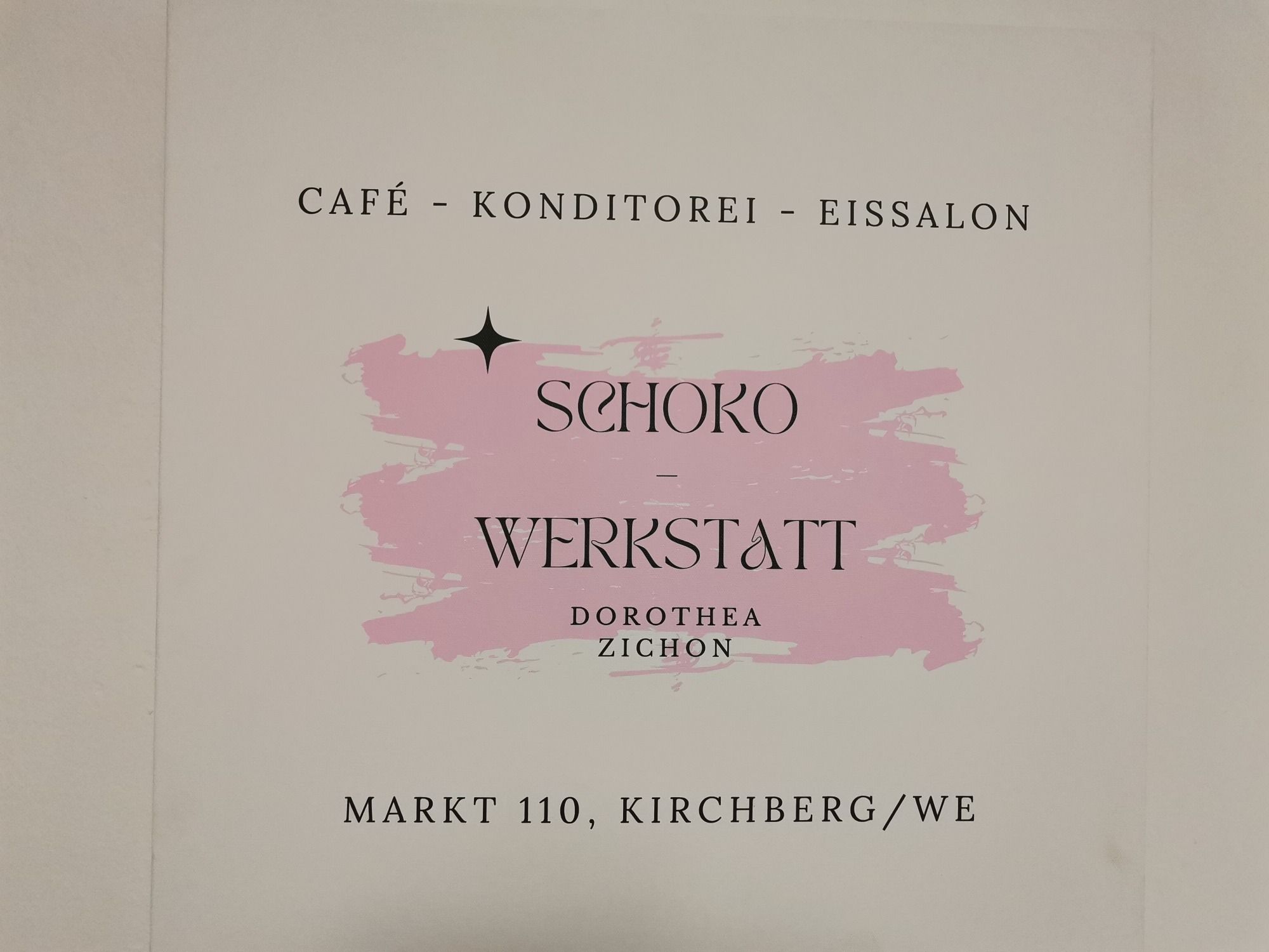 Sign for the chocolate workshop in Kirchberg with a pink background.