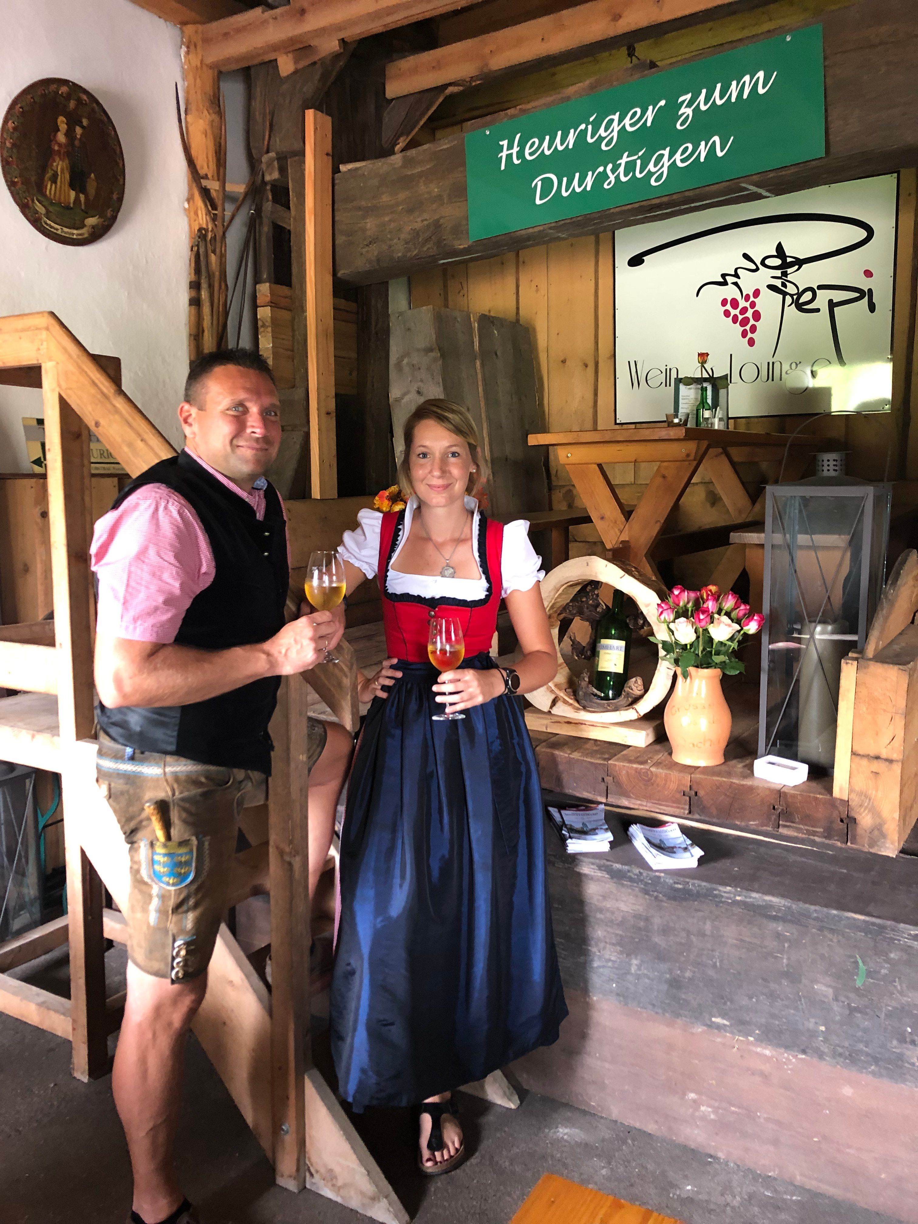 Two people in traditional dress at a wine tavern, with wine glasses in their hands.