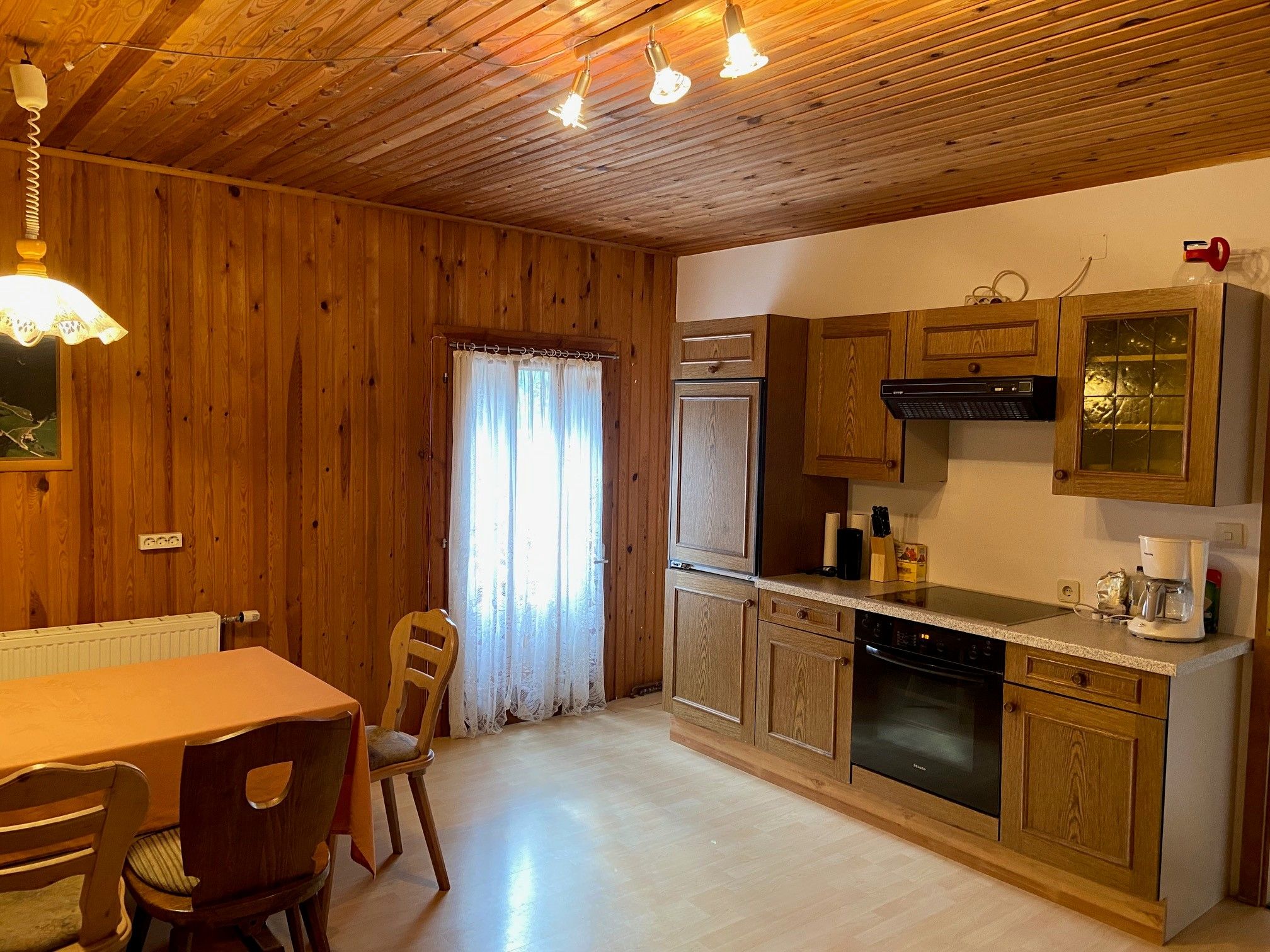 Rustic kitchen with wooden walls, dining table and chairs, and modern kitchen unit with appliances.