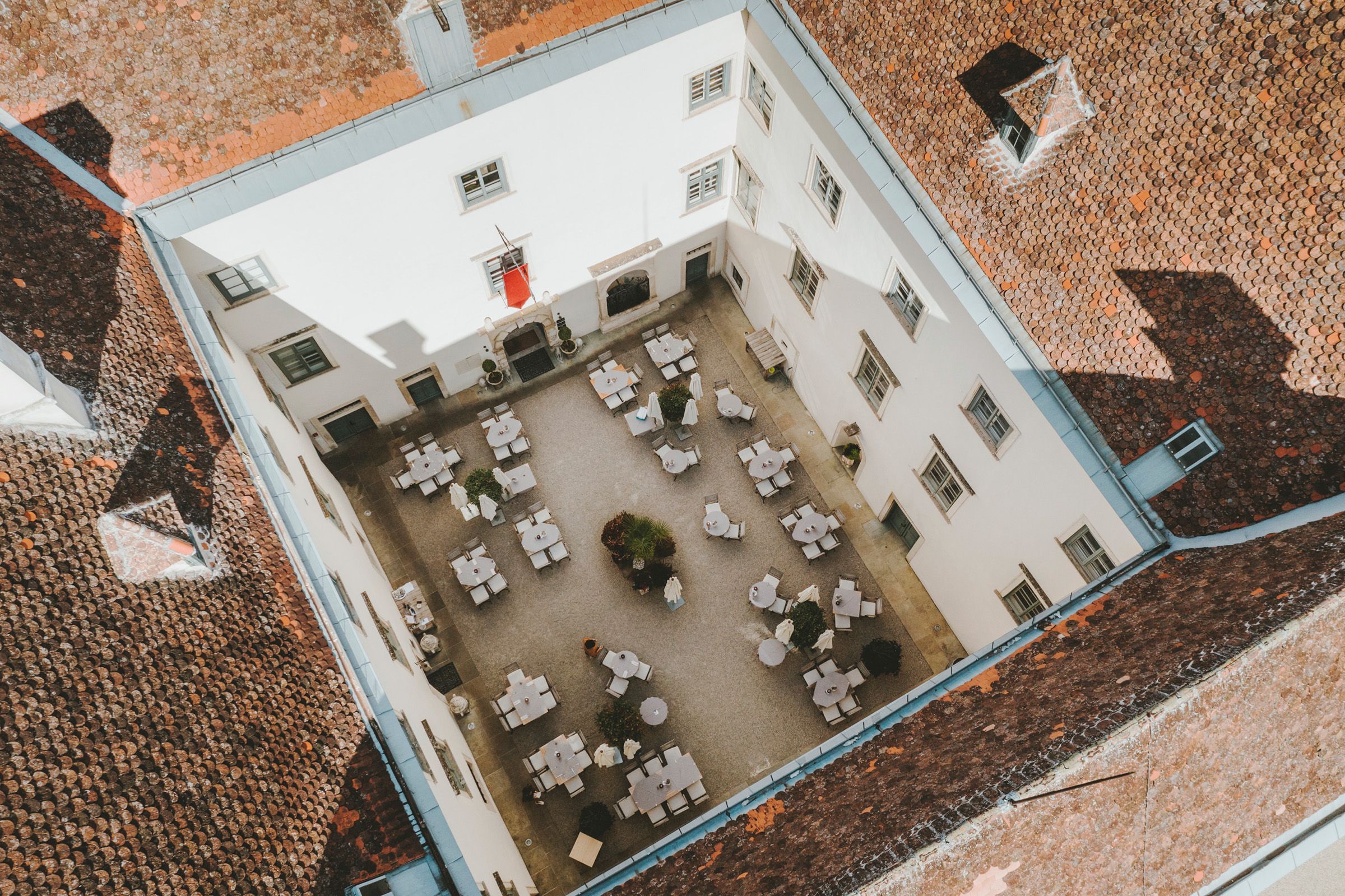 Aerial view of an inner courtyard with tables and chairs, surrounded by a building with red tiled roofs.