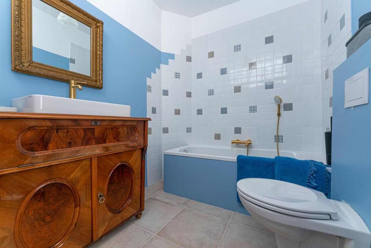 A bathroom with blue walls, a bathtub, a washbasin on a wooden cabinet and a golden mirror.
